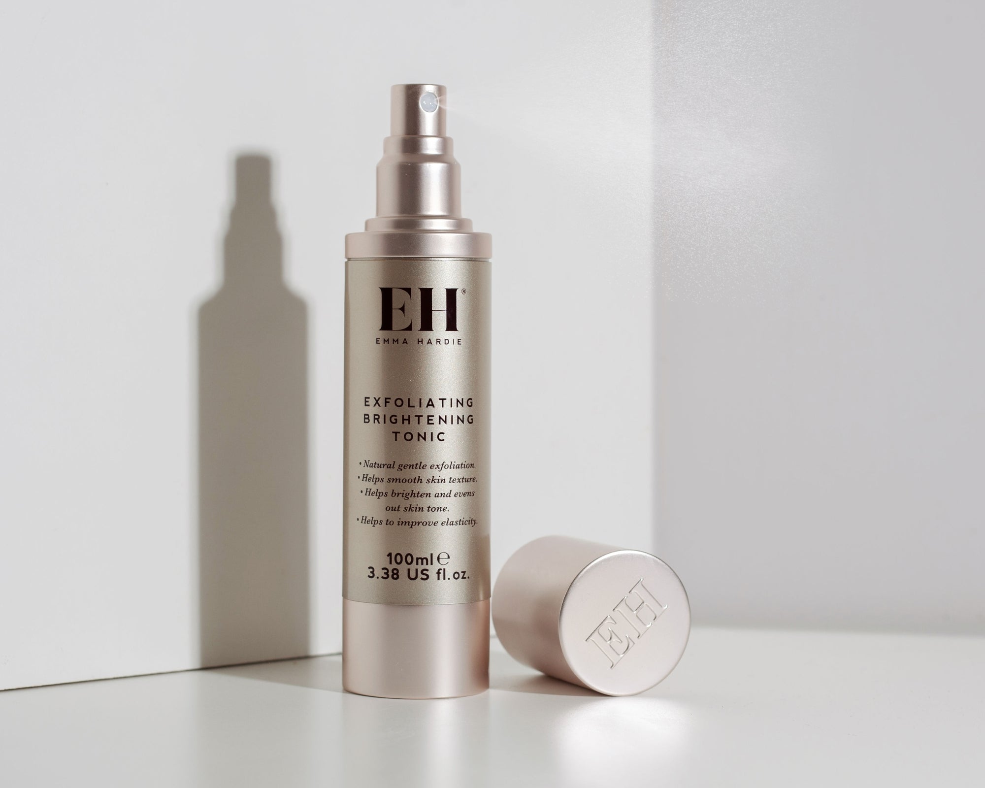 A bottle of Emma Hardie Exfoliating Brightening Tonic with its cap off, displayed on a clean white surface with a soft shadow cast to the left.