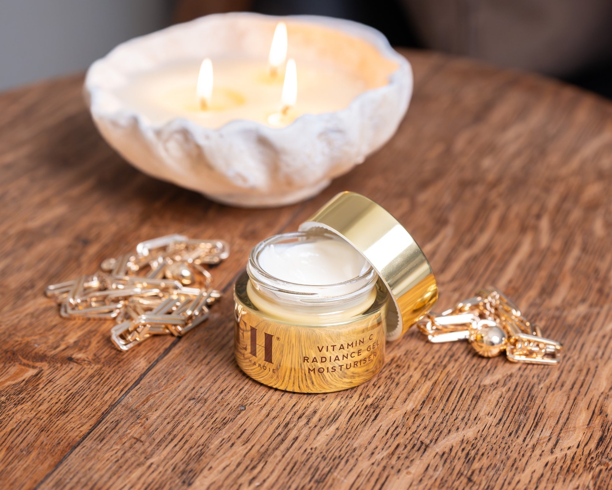 Emma Hardie Vitamin C Radiance Gel Moisturiser open on a wooden table beside a lit candle and gold accessories.