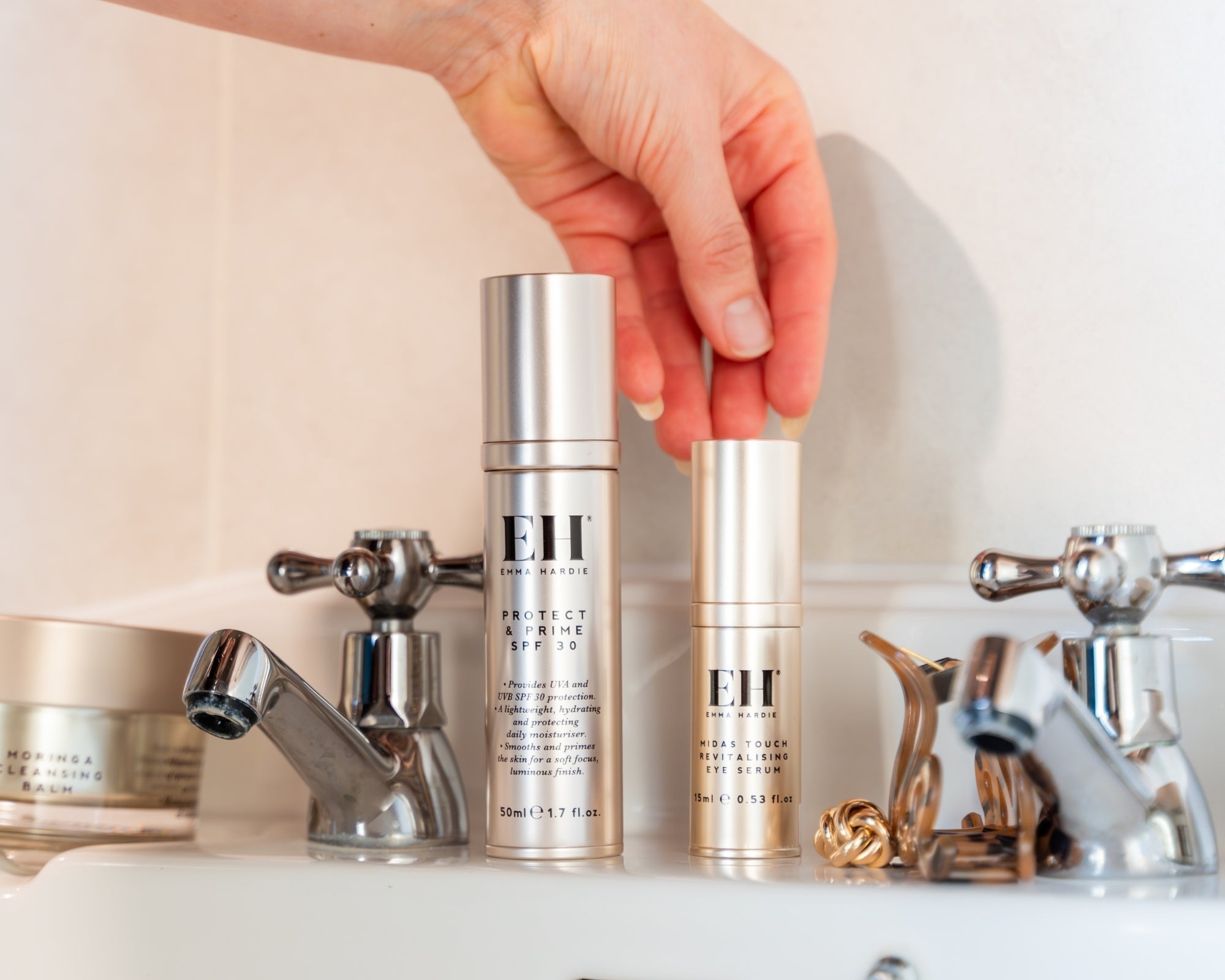 Emma Hardie Protect & Prime SPF30 and Midas Touch Revitalising Eye Serum displayed on a bathroom sink, with Moringa Cleansing Balm in the background.