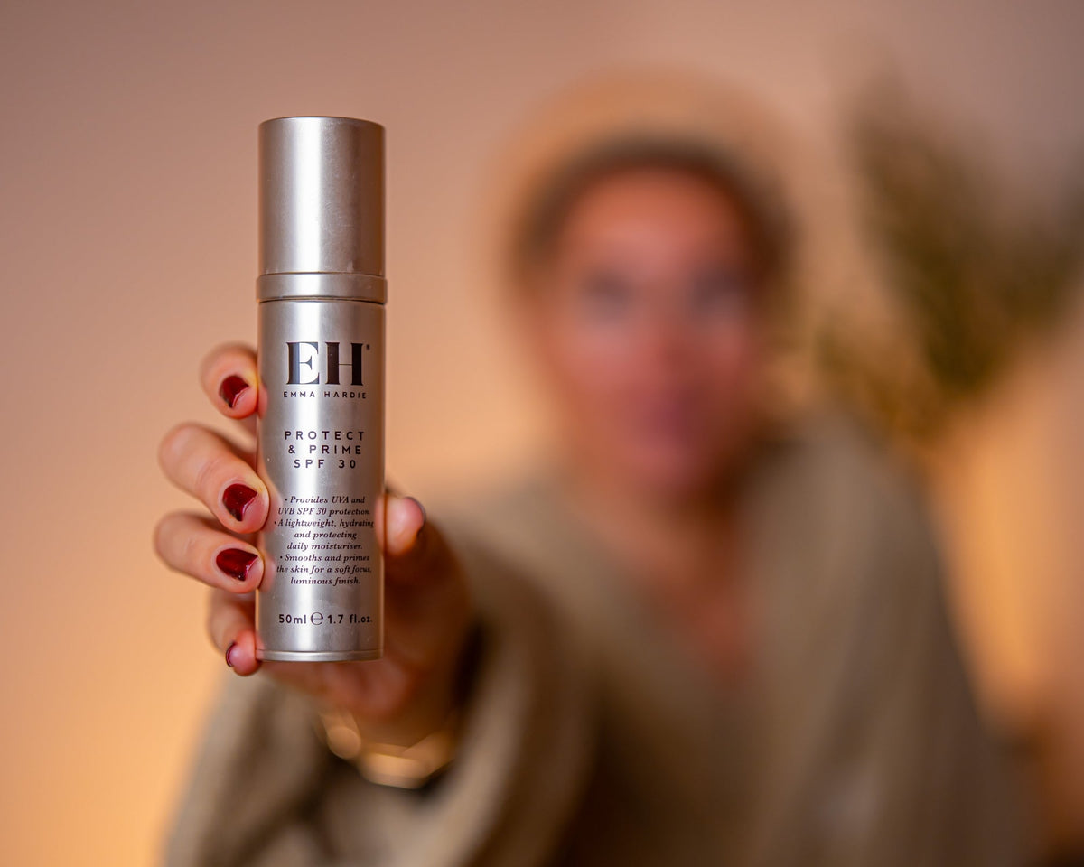 Woman holding Emma Hardie Protect & Prime SPF 30 towards the camera, with a softly blurred background.
