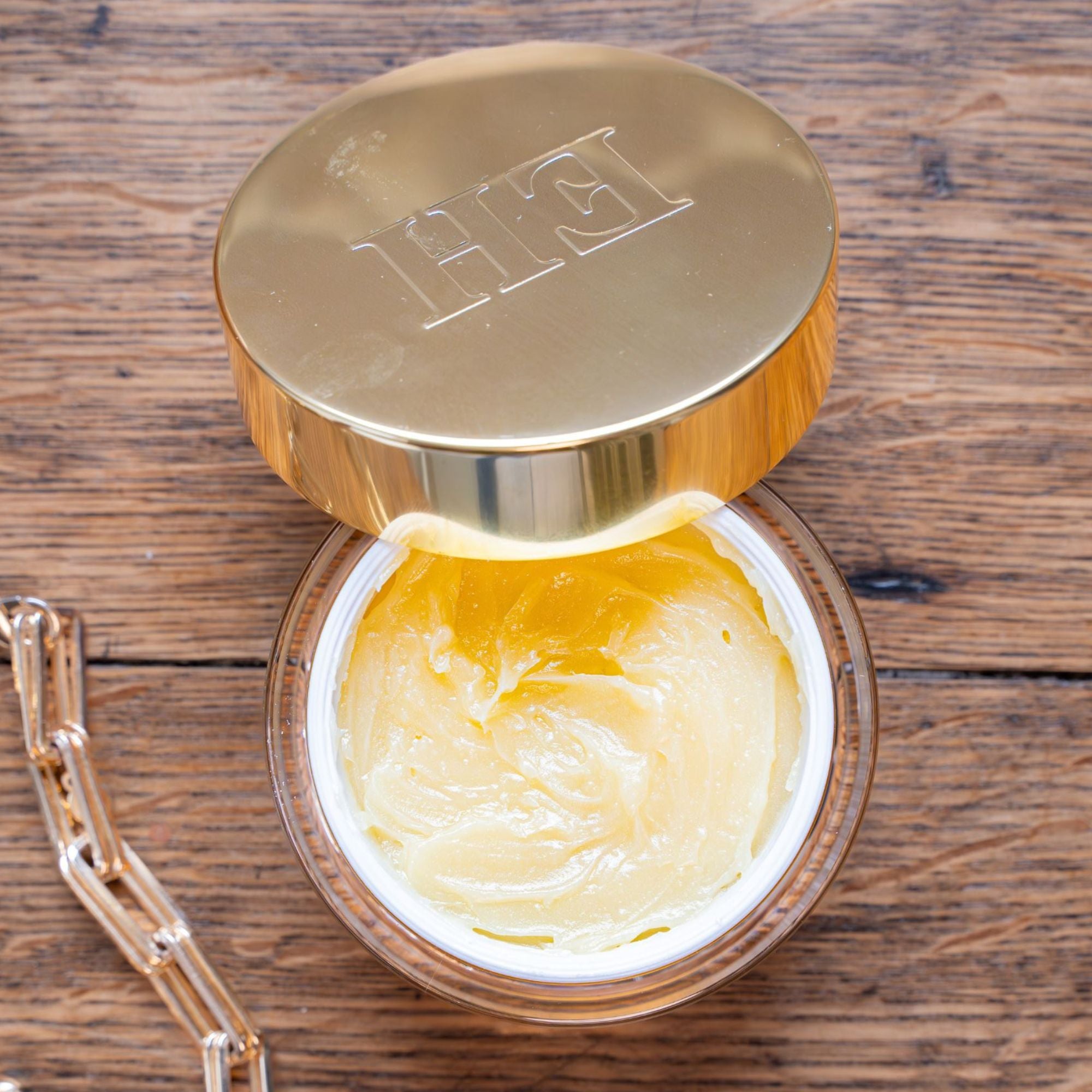 Open jar of Emma Hardie Moringa Cleansing Balm with gold lid, showing the rich balm texture on a wooden surface.