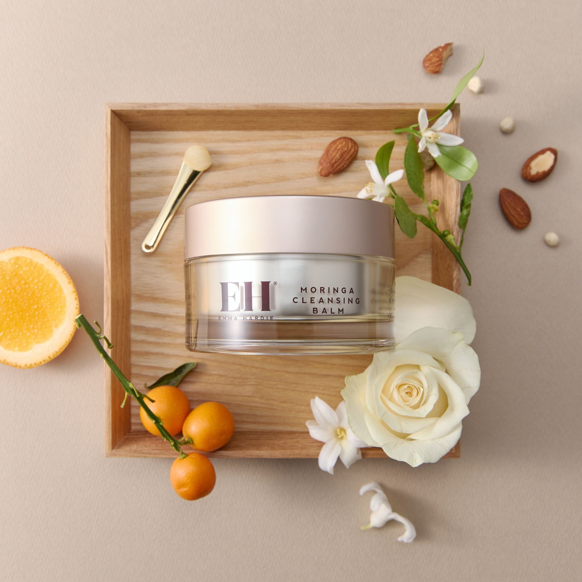 Jar of Emma Hardie Moringa Cleansing Balm on a wooden tray with flowers and fruits on a beige background