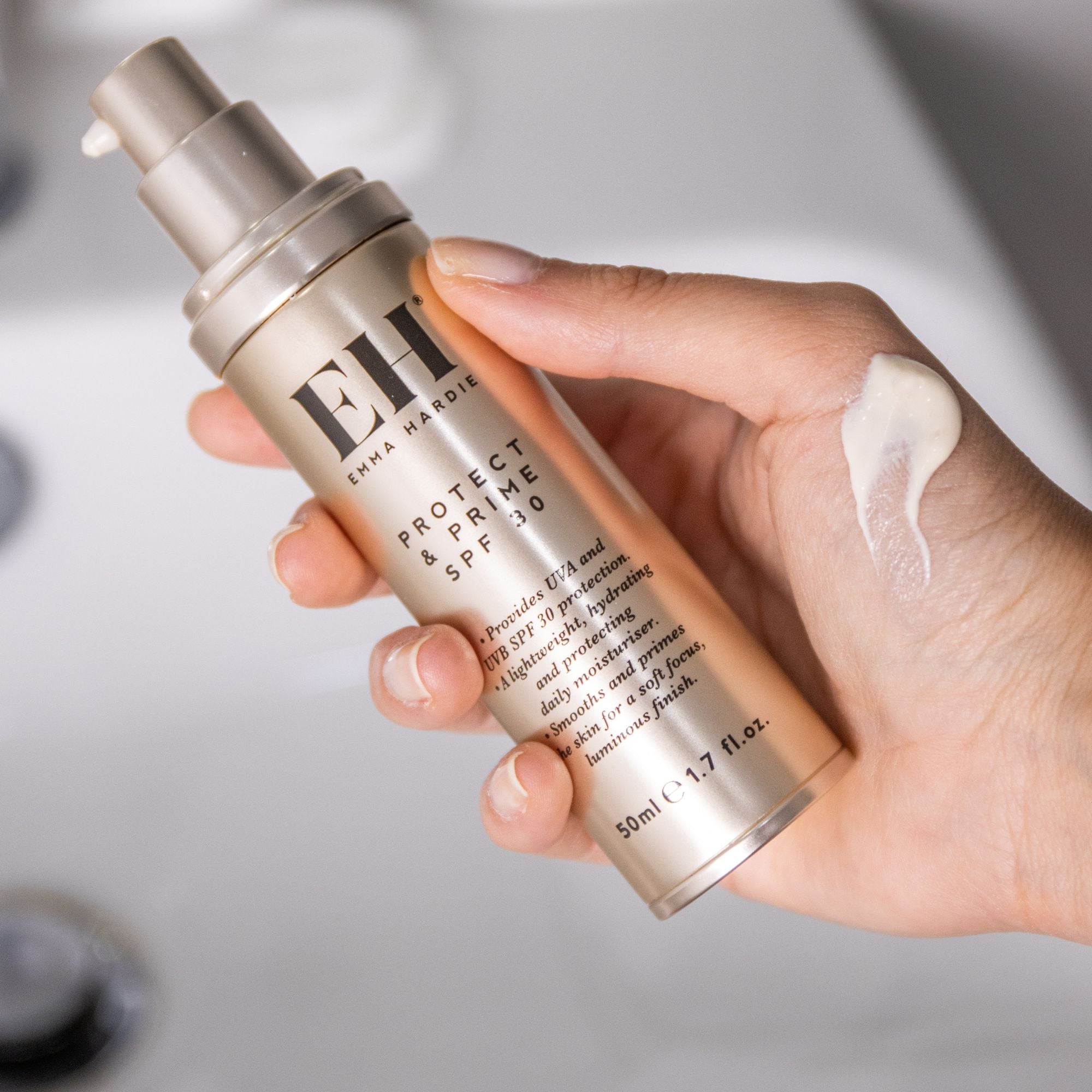Hand holding a tube of Emma Hardie Protect & Prime SPF 30 with a swatch of the product, against a neutral background