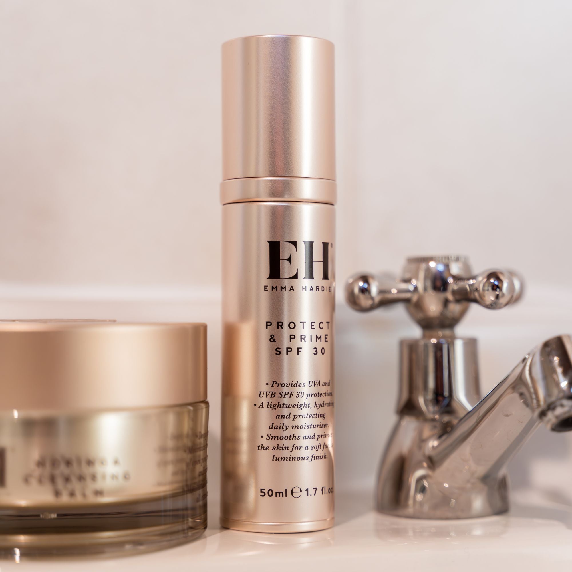 Emma Hardie Protect & Prime SPF30 bottle displayed beside Moringa Cleansing Balm and a chrome bathroom tap.