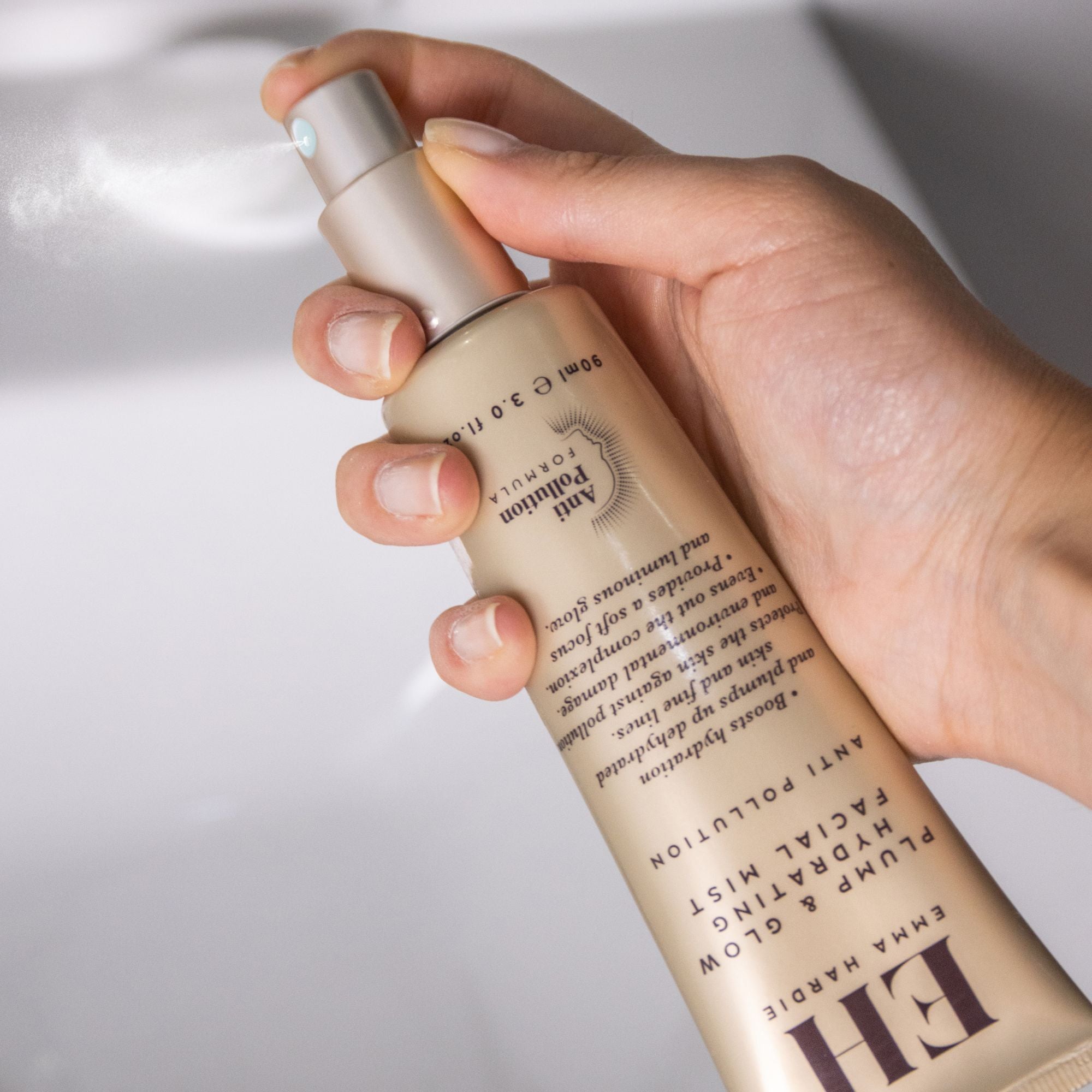 Hand spraying Emma Hardie Plump & Glow Hydrating Facial Mist, creating a fine mist to refresh and hydrate the skin.