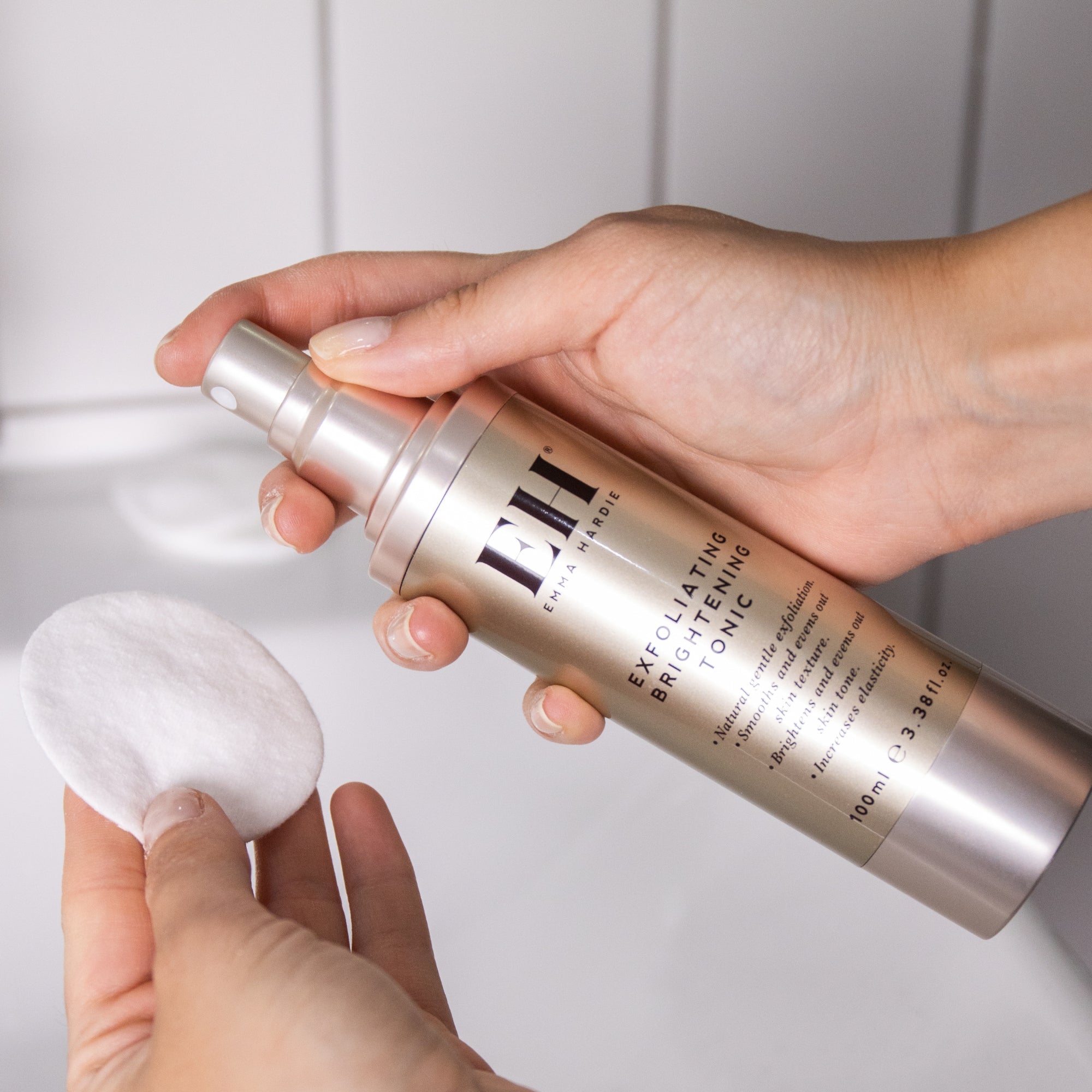 Hands applying Emma Hardie Exfoliating Brightening Tonic onto a cotton pad, ready to sweep over cleansed skin.