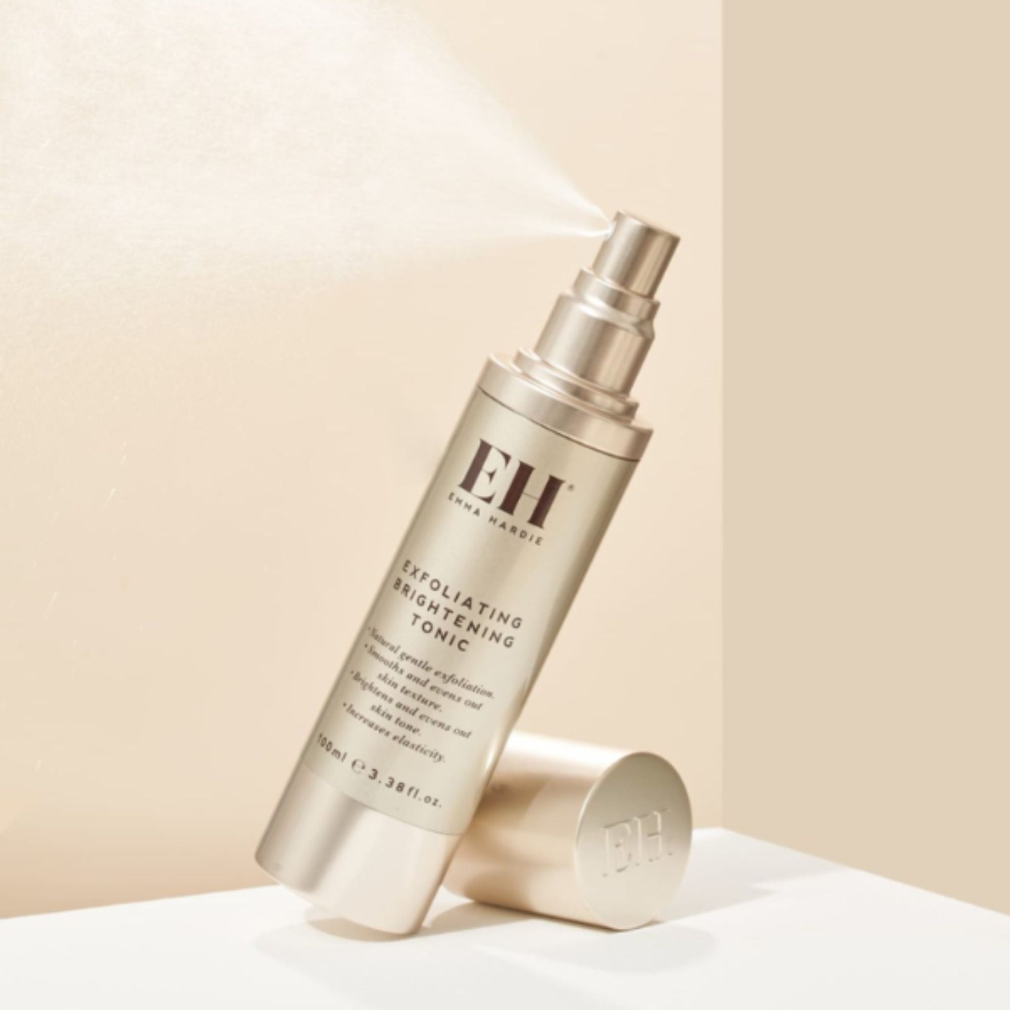 Emma Hardie Exfoliating Brightening Tonic bottle spraying a fine mist against a soft neutral background, with the cap placed beside it.
