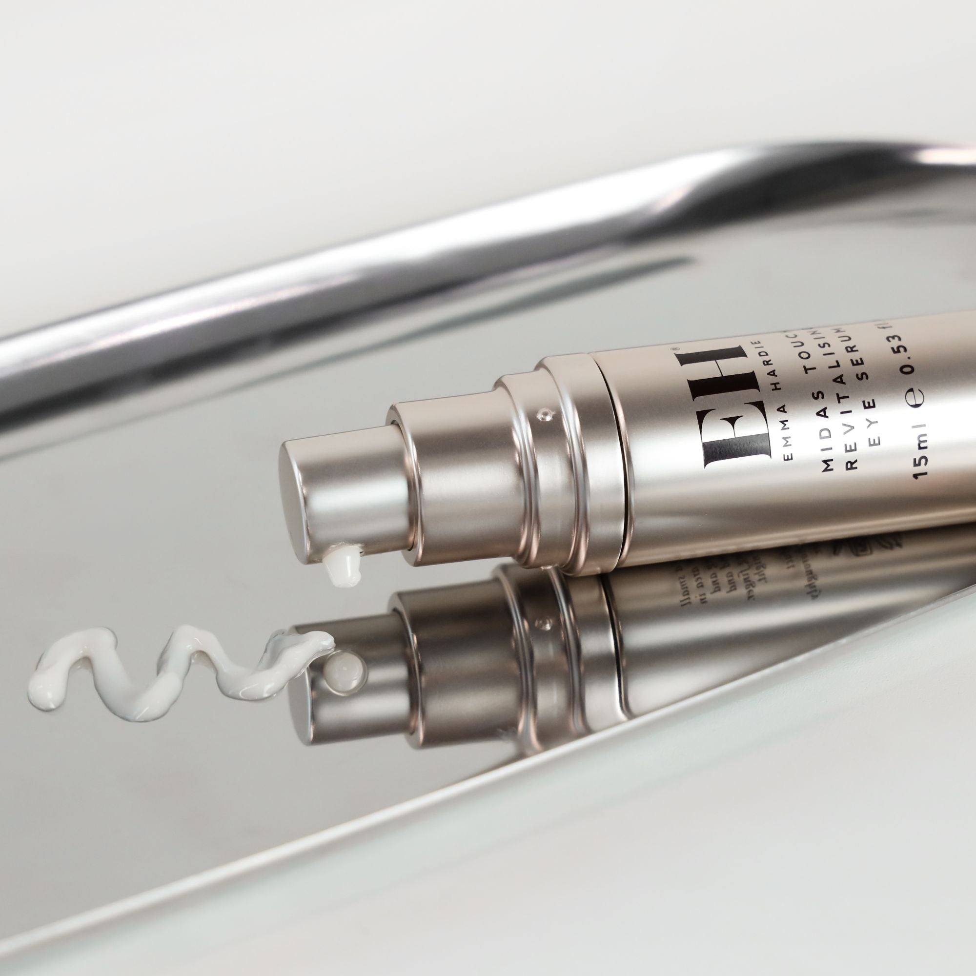 Emma Hardie Midas Touch Revitalising Eye Serum lying on a reflective tray, with a small amount of cream dispensed beside it.
