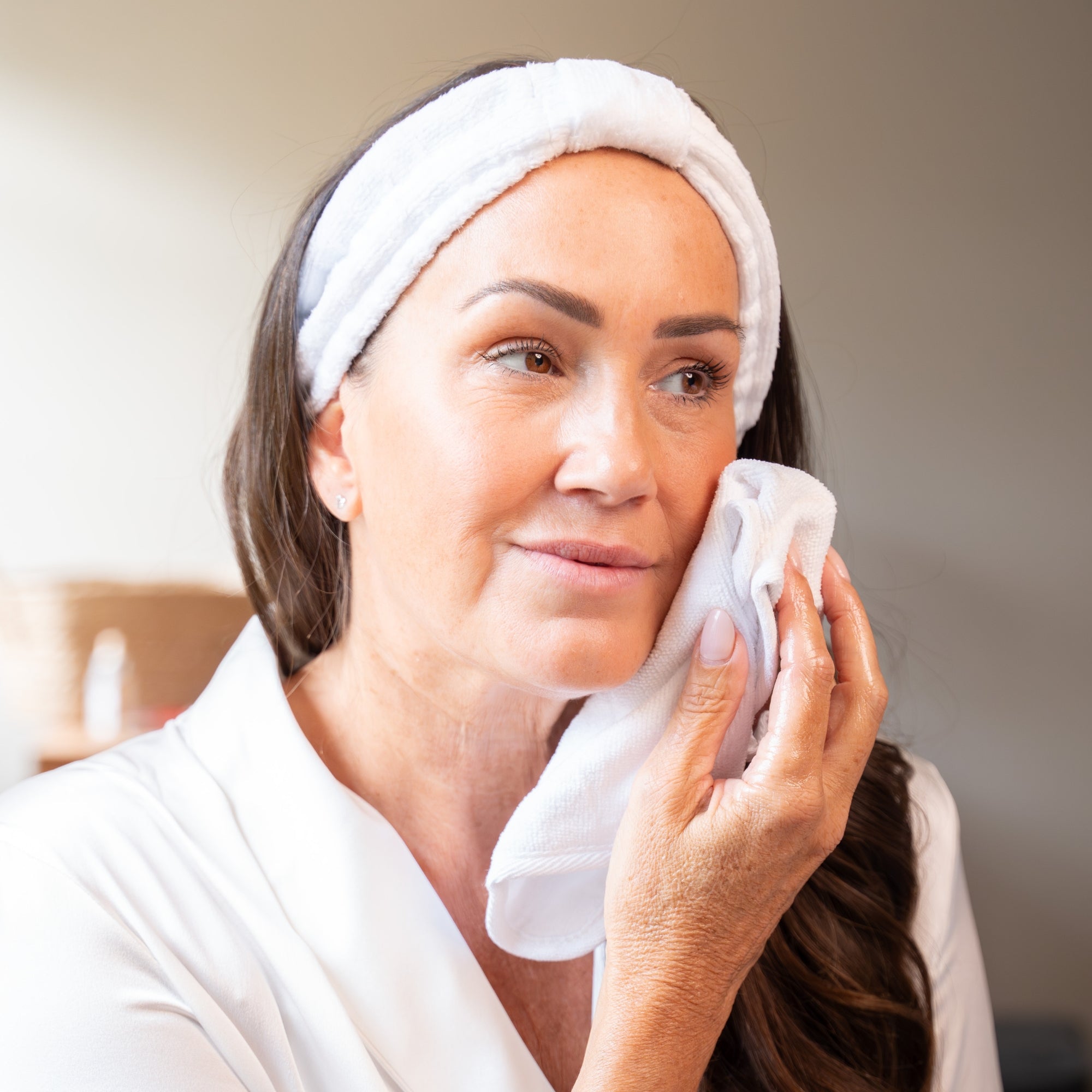 Woman in a white robe and headband cleaning her face with an Emma Hardie dual action cleansing cloth.