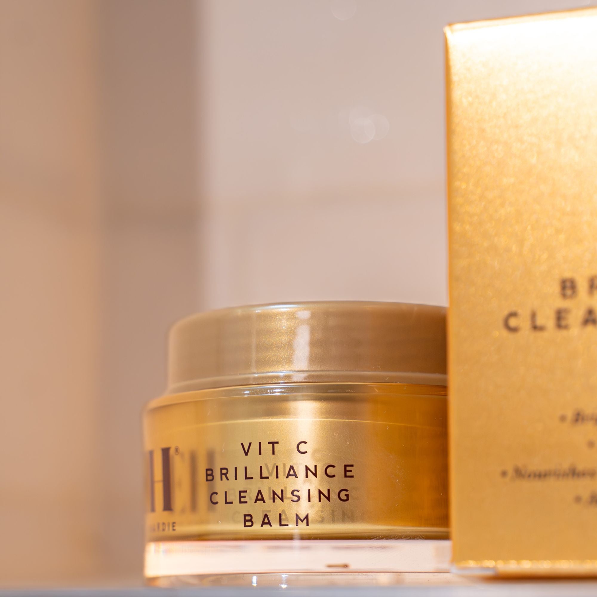 Vit C Brilliance Cleansing Balm jar with gold lid on a neutral background
