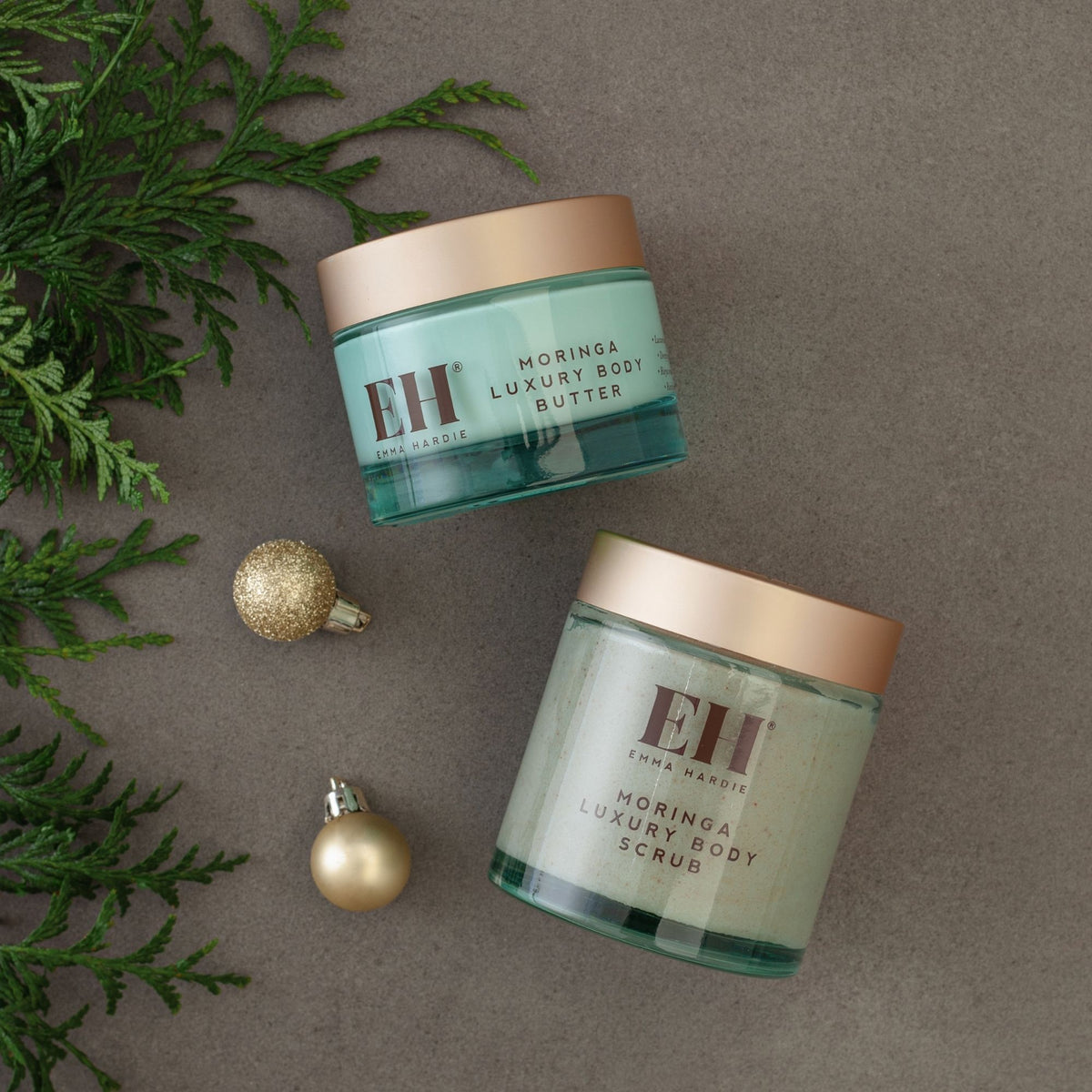 Emma Hardie Moringa Luxury Body Butter and Body Scrub on a stone background with festive greenery and gold baubles.