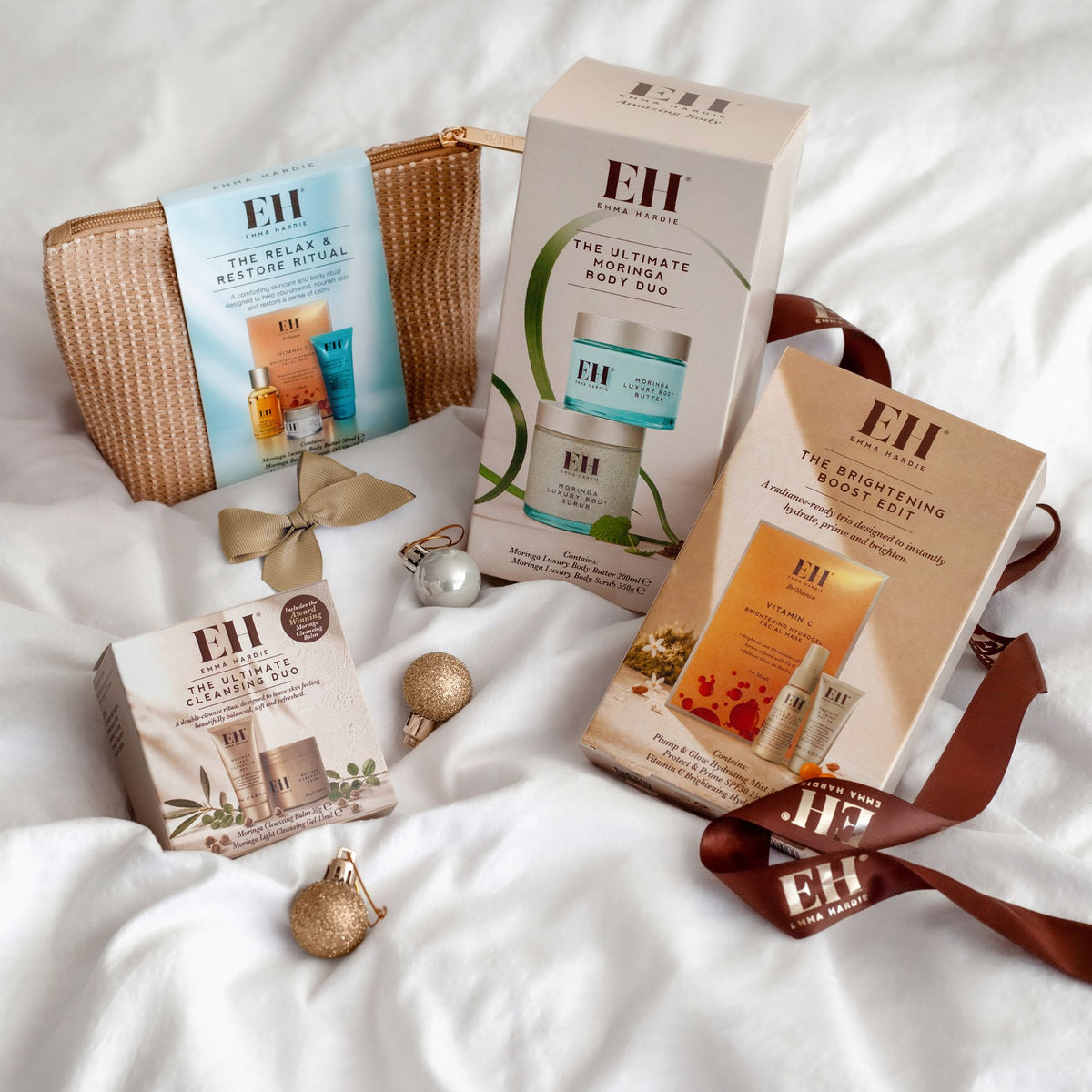 Emma Hardie Christmas gifts on white fabric, featuring the Relax & Restore Ritual, Ultimate Moringa Body Duo, Brightening Boost Edit and Ultimate Cleansing Duo, with festive baubles and ribbon.