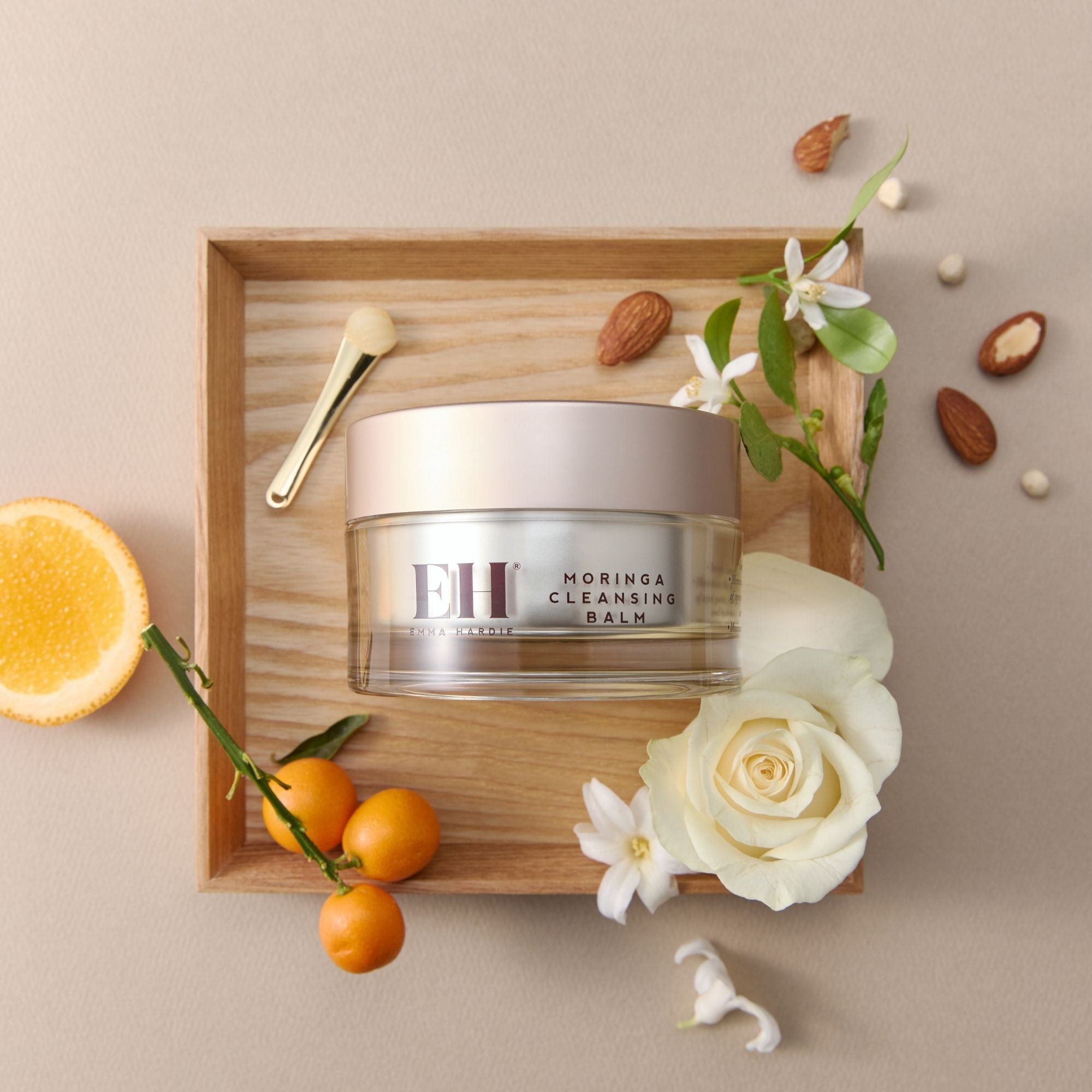 Emma Hardie Moringa cleansing balm jar on a wooden tray with fruits and flowers on a beige background