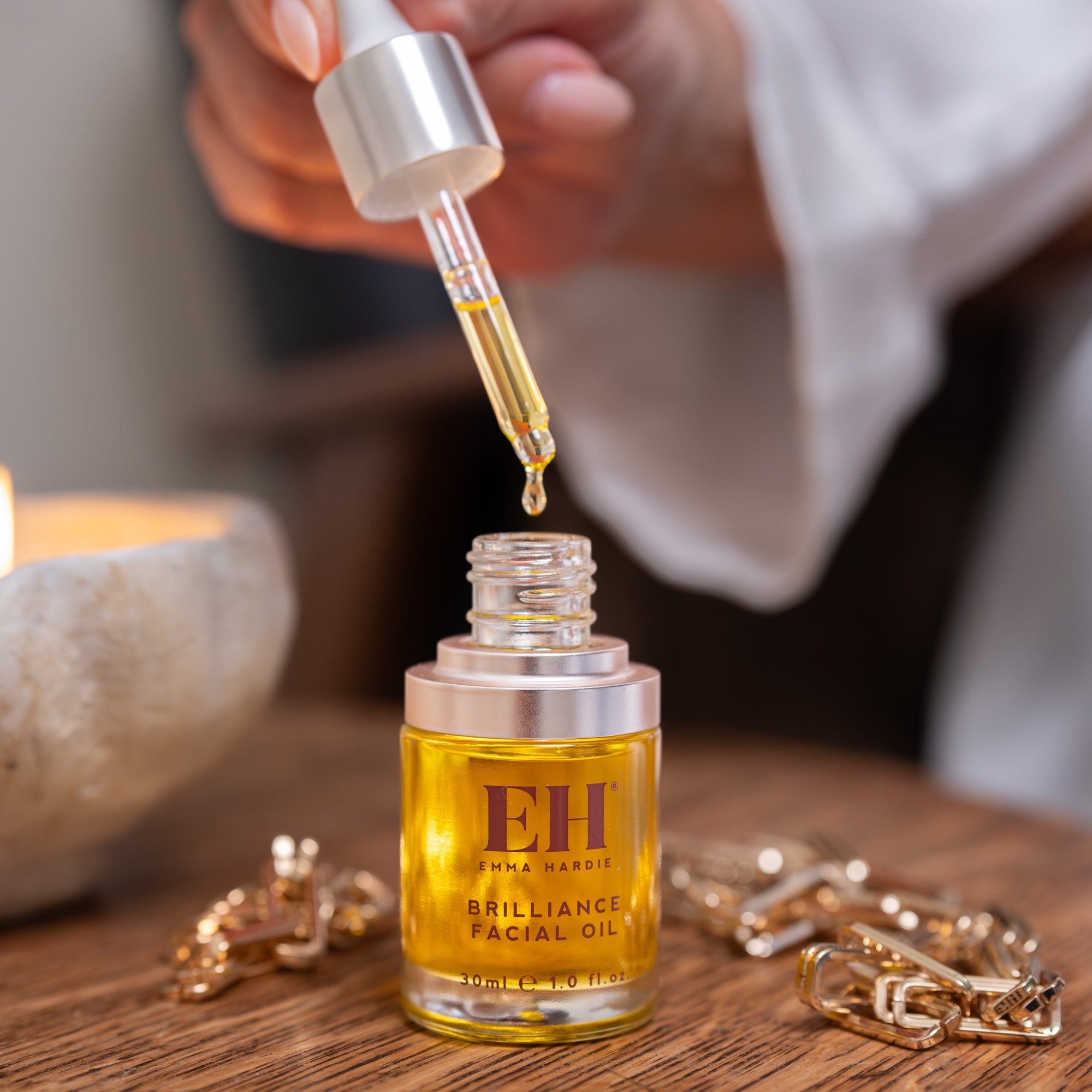 Hand using a dropper to add oil from a bottle labeled 'EH' onto a wooden surface.