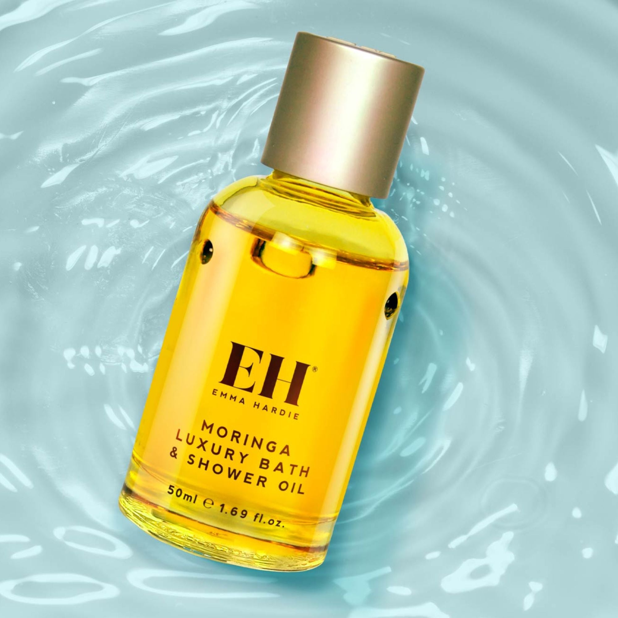 Bottle of Emma Hardie Moringa Luxury Bath & Shower Oil on a light blue background