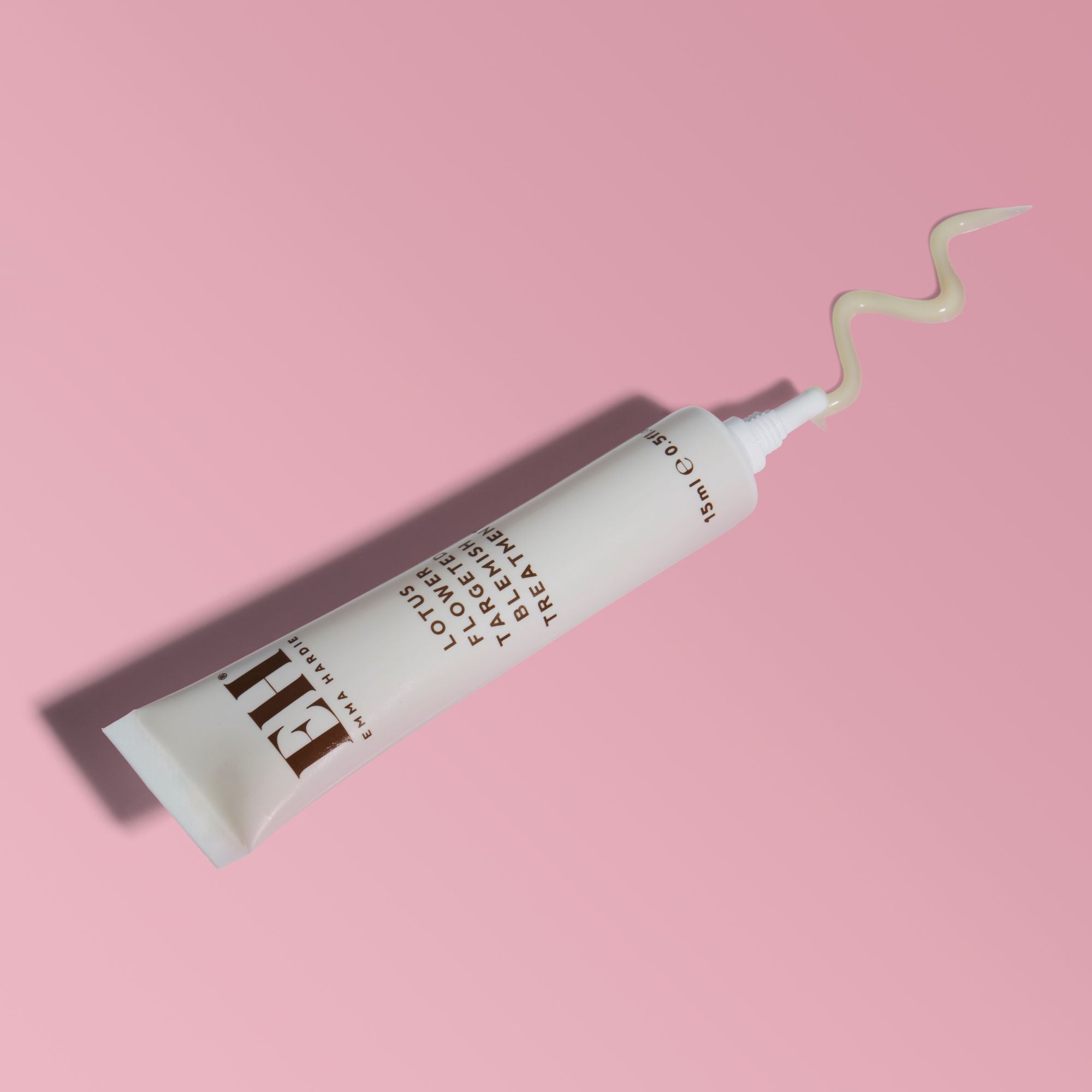 Emma Hardie Lotus Flower Targeted Blemish Treatment tube on a soft pink background, with product texture dispensed from the nozzle.