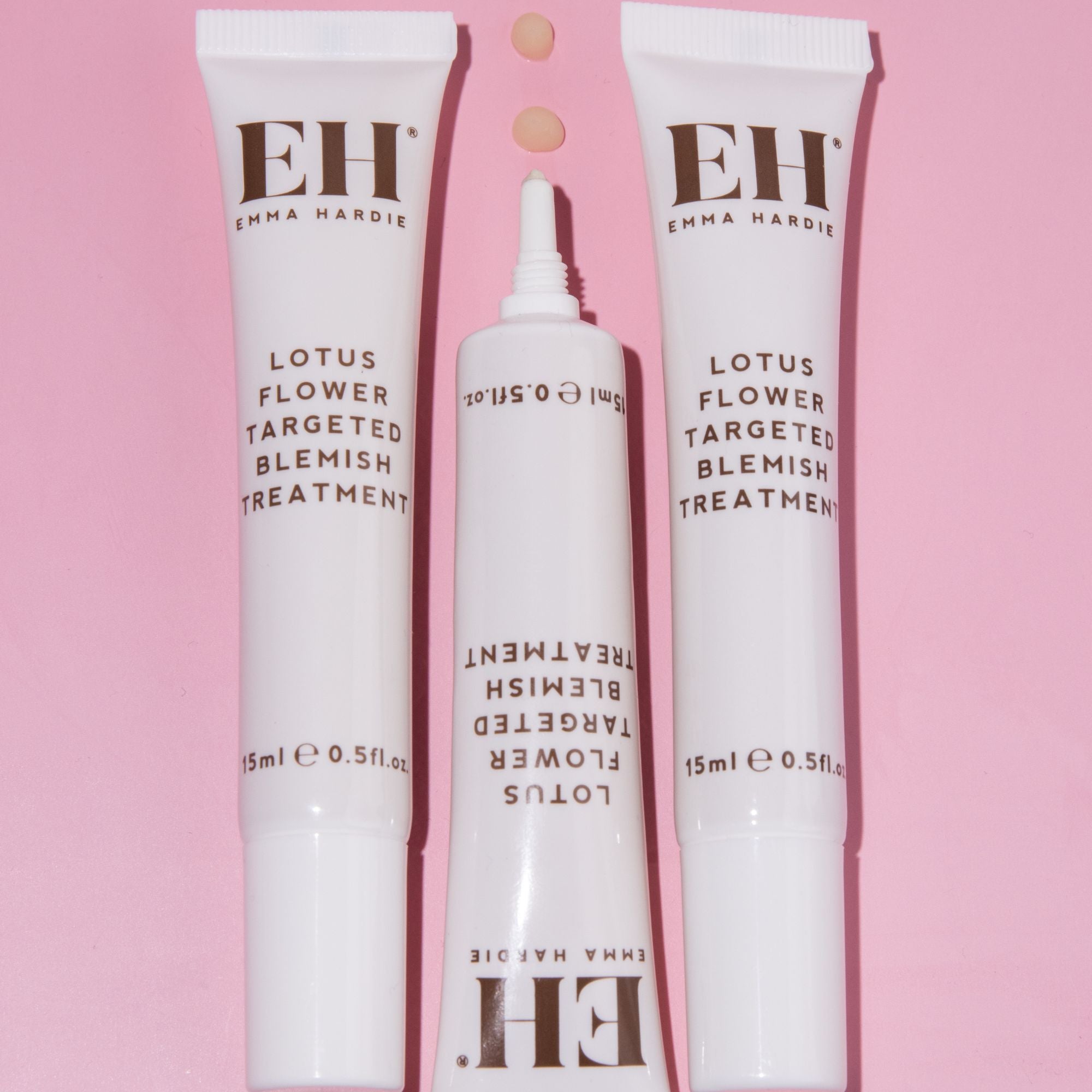 Emma Hardie Lotus Flower Targeted Blemish Treatment tubes on a soft pink background, with small product texture droplets shown above.