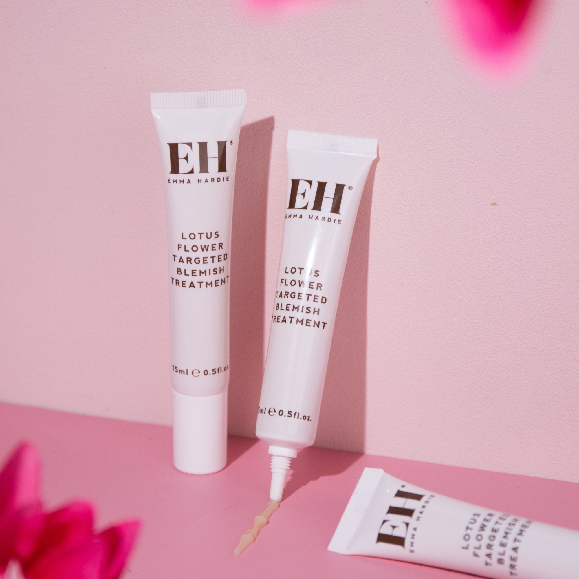 Emma Hardie Lotus Flower Targeted Blemish Treatment tubes on a soft pink background, with product texture dispensed from one nozzle.