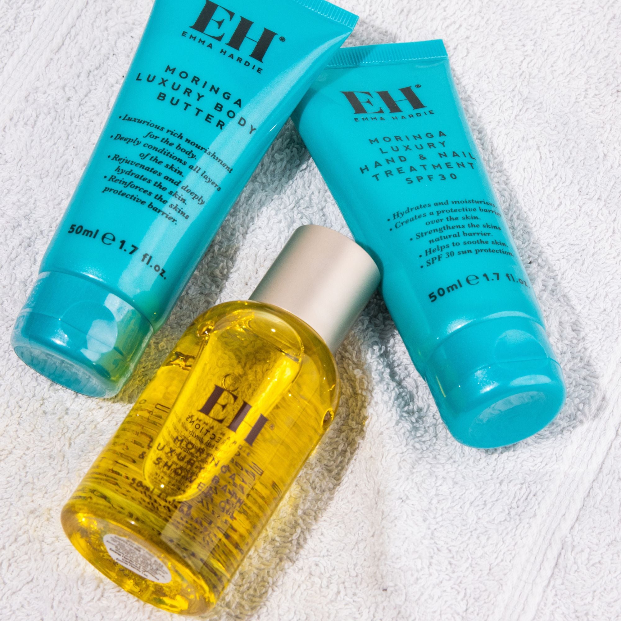Emma Hardie Moringa body care collection with Luxury Body Butter, Luxury Hand and Nail Treatment SPF30 and Luxury Bath & Shower Oil on a soft white towel.