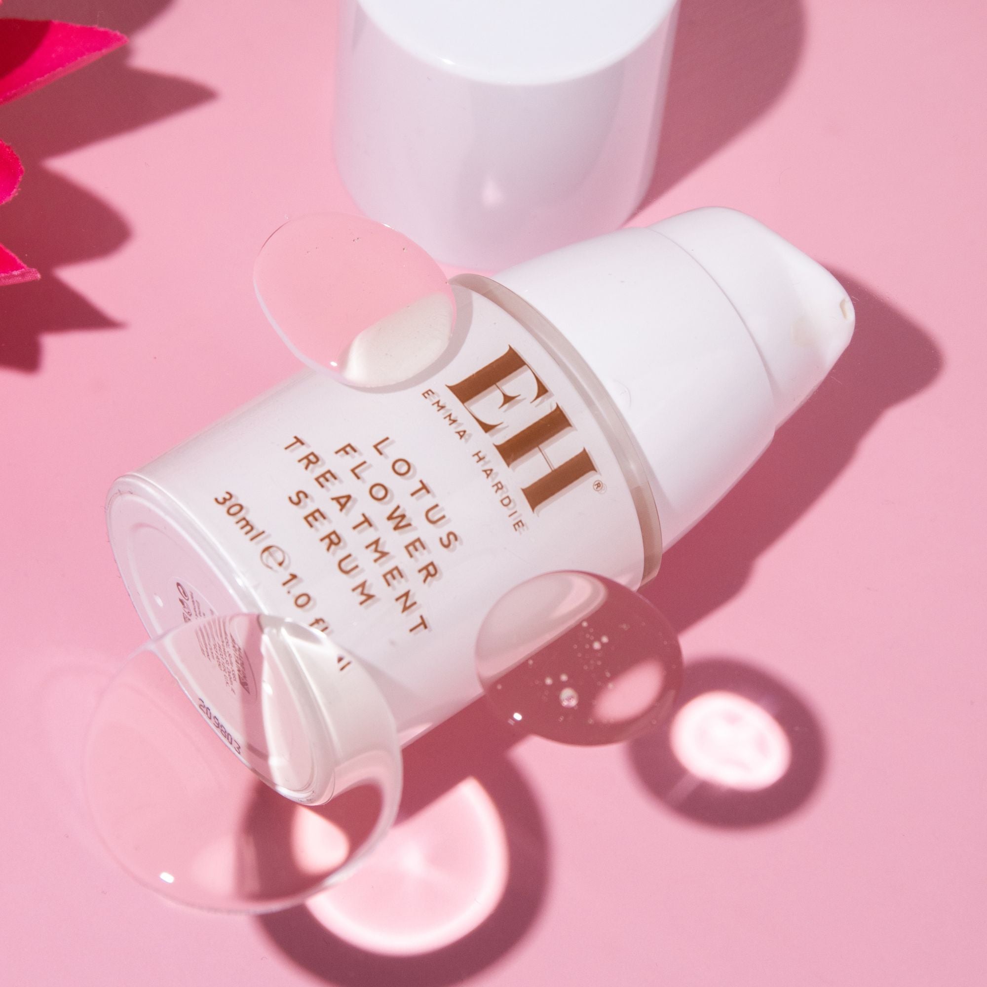 Emma Hardie Lotus Flower Treatment Serum bottle on a soft pink background, styled with clear droplet accents.