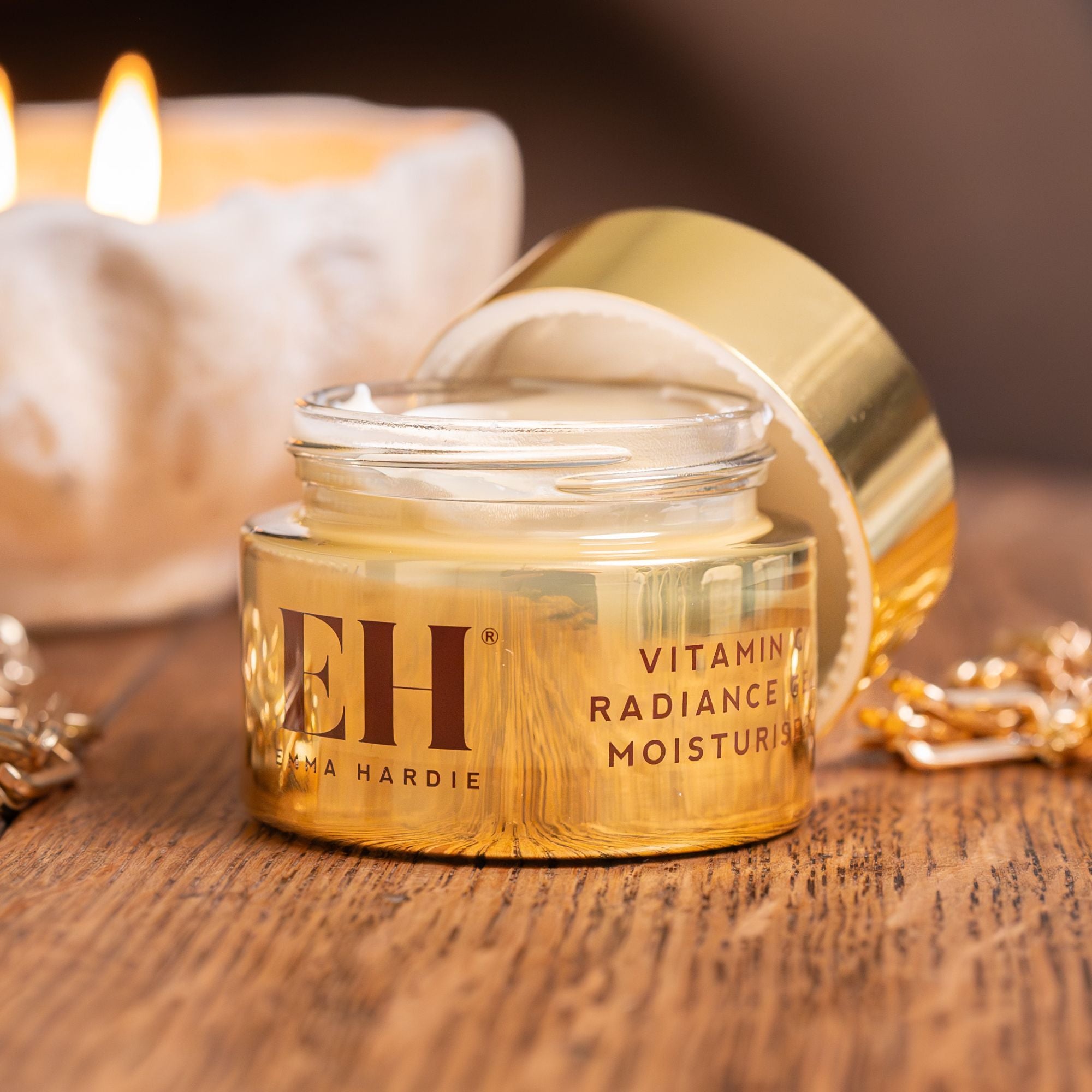 Open jar of Emma Hardie Vitamin C Radiance Gel Moisturiser on a wooden surface, styled with a gold chain and softly lit candle in the background.
