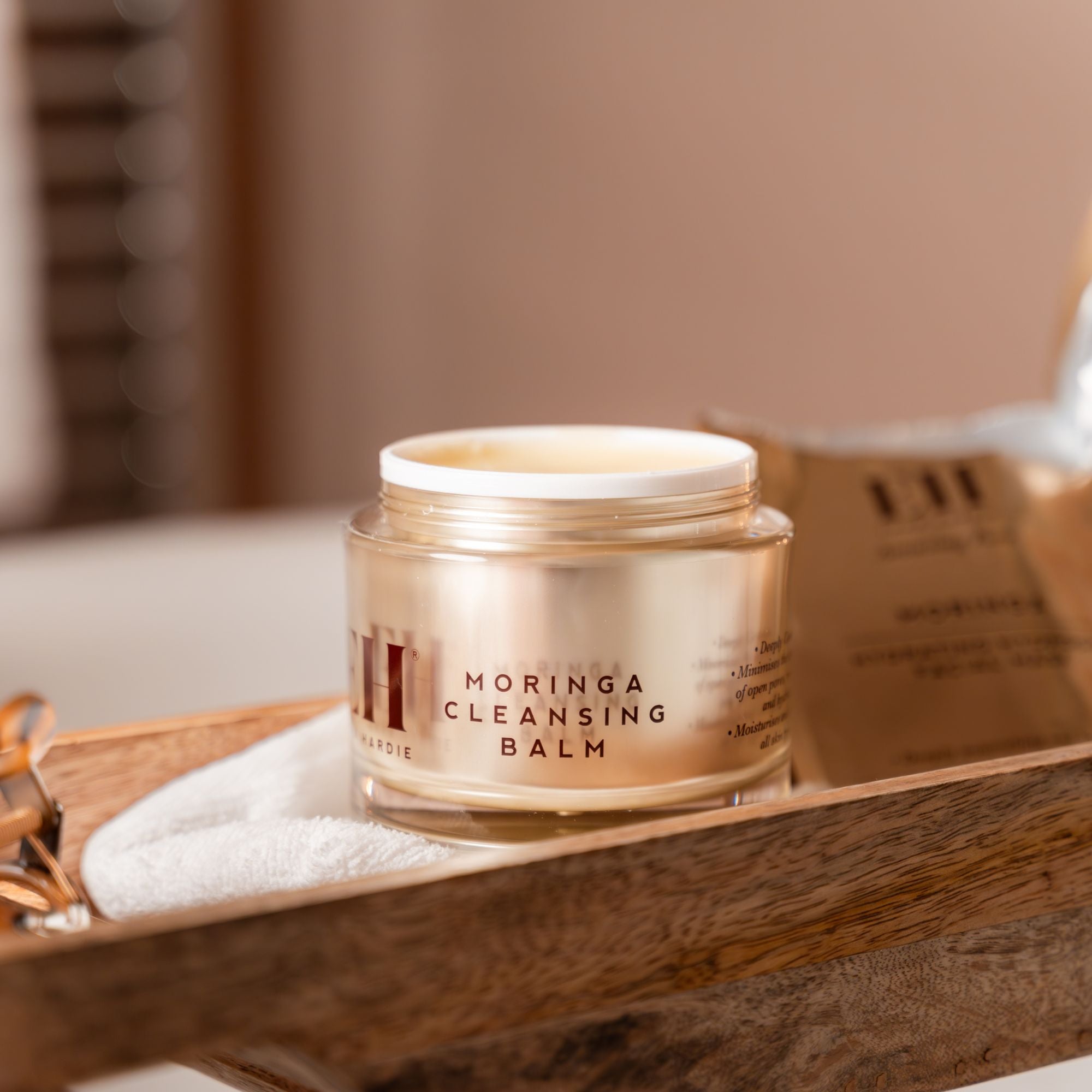 Jar of Moringa Cleansing Balm on a wooden tray with a blurred background