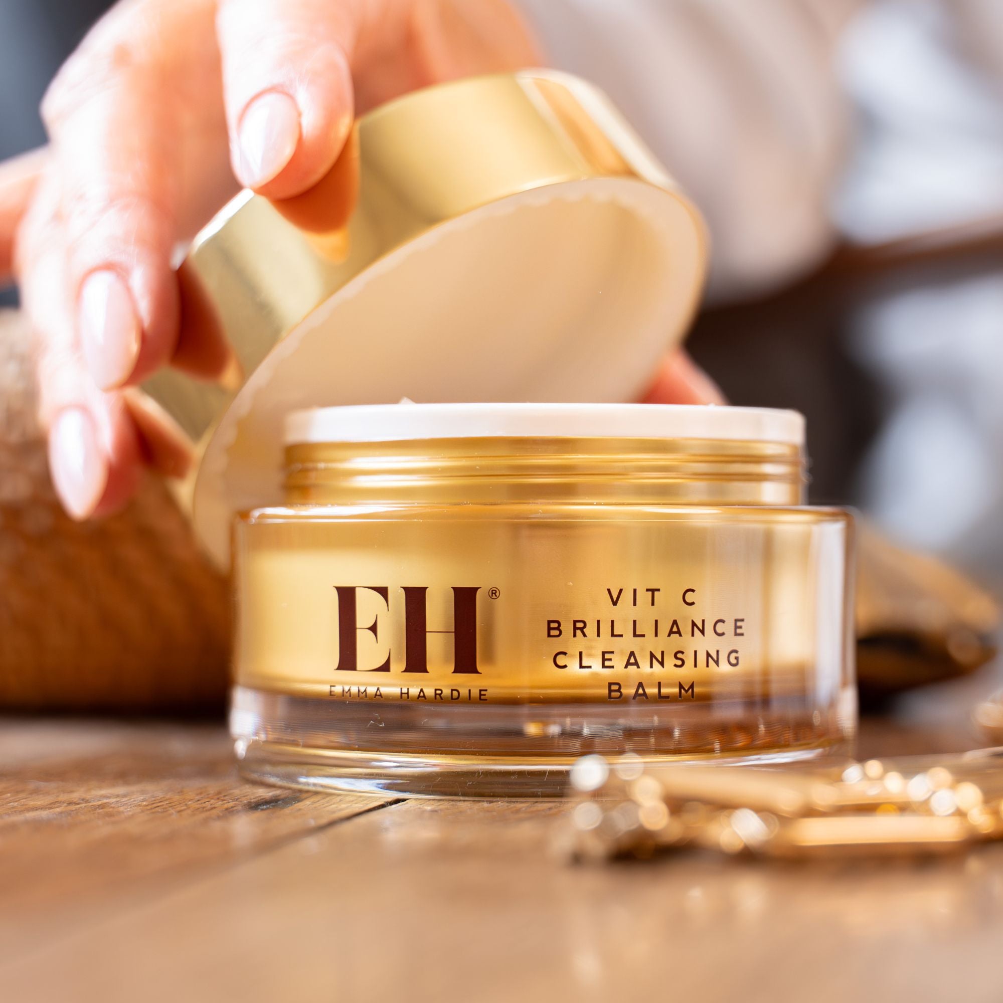 Emma Haride Vit C Brilliance Cleansing Balm with open gold lid on a wooden surface