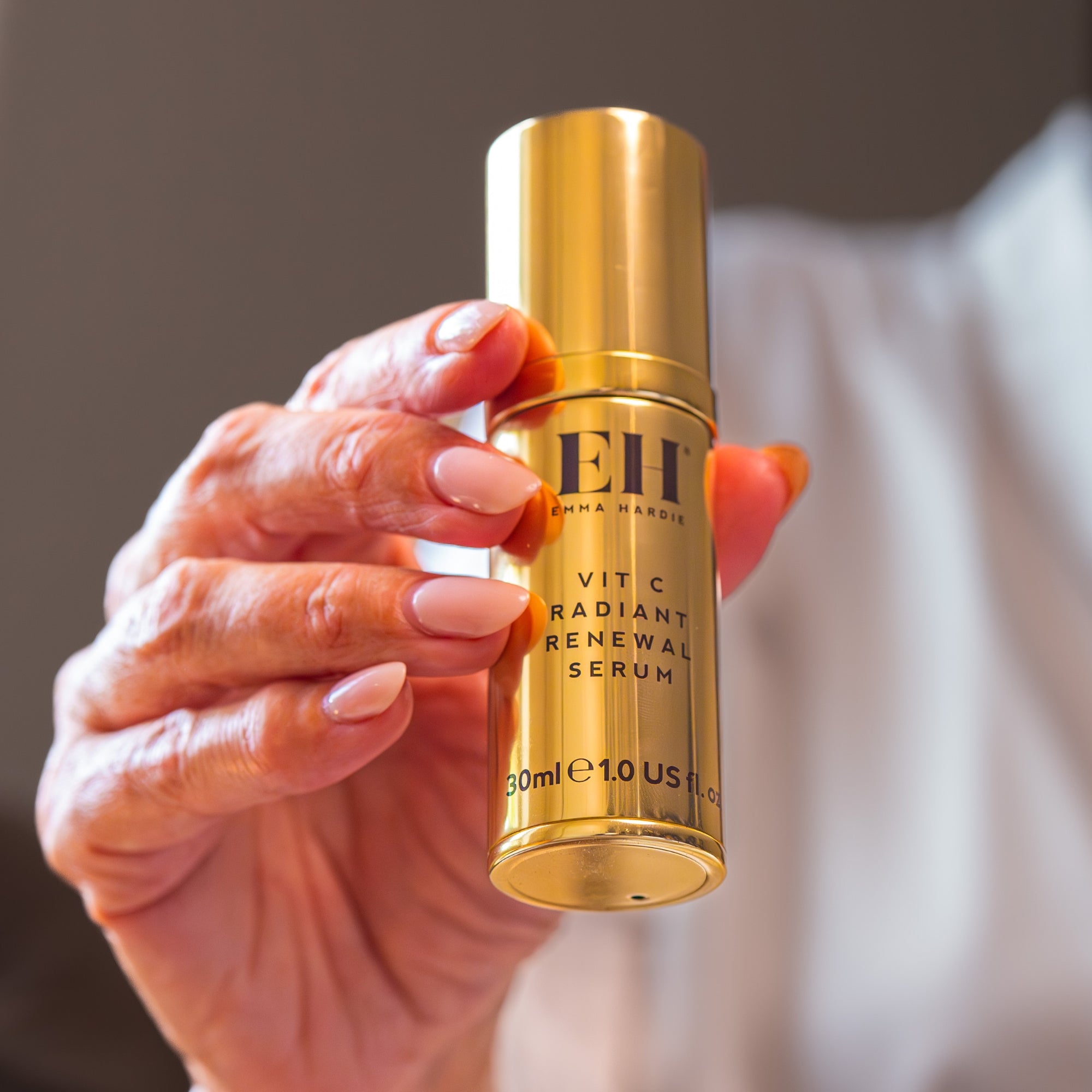Gold Vit C Radiant Renewal Serum bottle held by a hand with neutral nail polish.