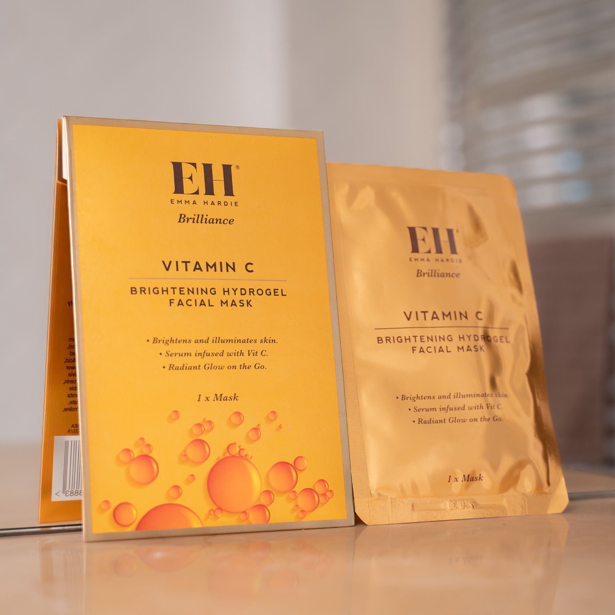 Emma Hardie Vitamin C Brightening Hydrogel Facial Mask packaging and sachet displayed together on a reflective surface.