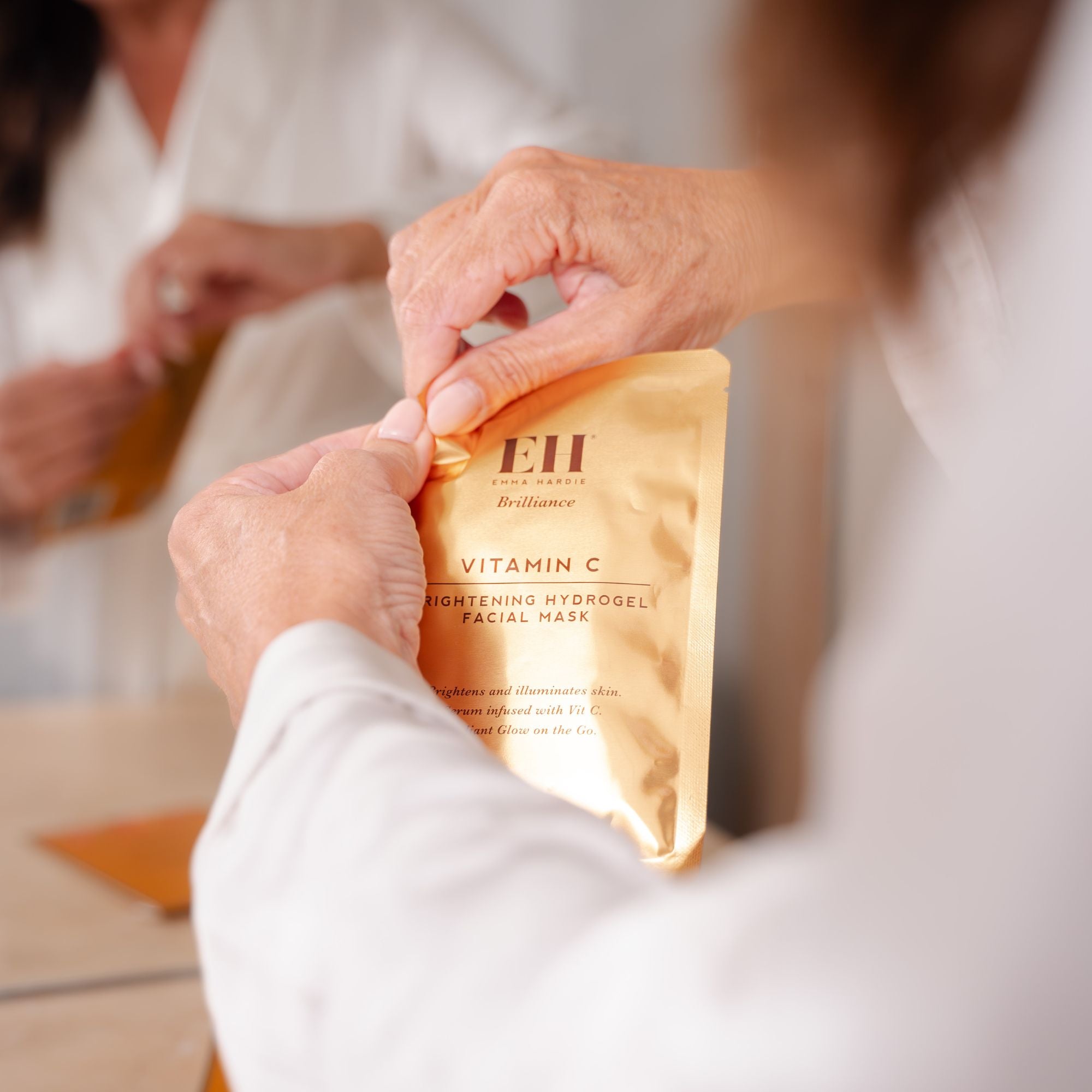 Hands opening an Emma Hardie Vitamin C Brightening Hydrogel Facial Mask sachet during a skincare routine.