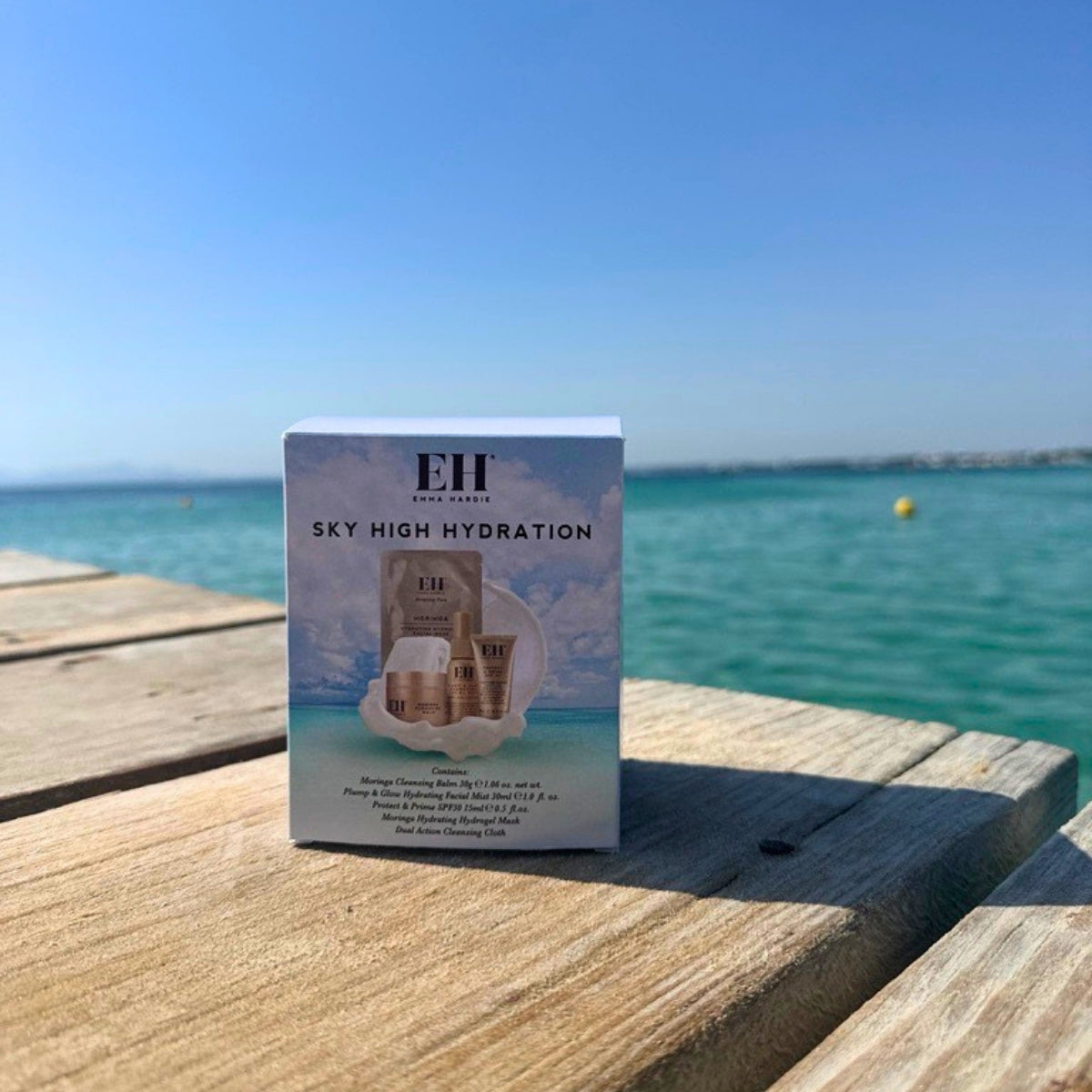 Emma Hardie Sky High Hydration skincare set on a wooden deck by the sea, featuring travel-size hydration and cleansing essentials.