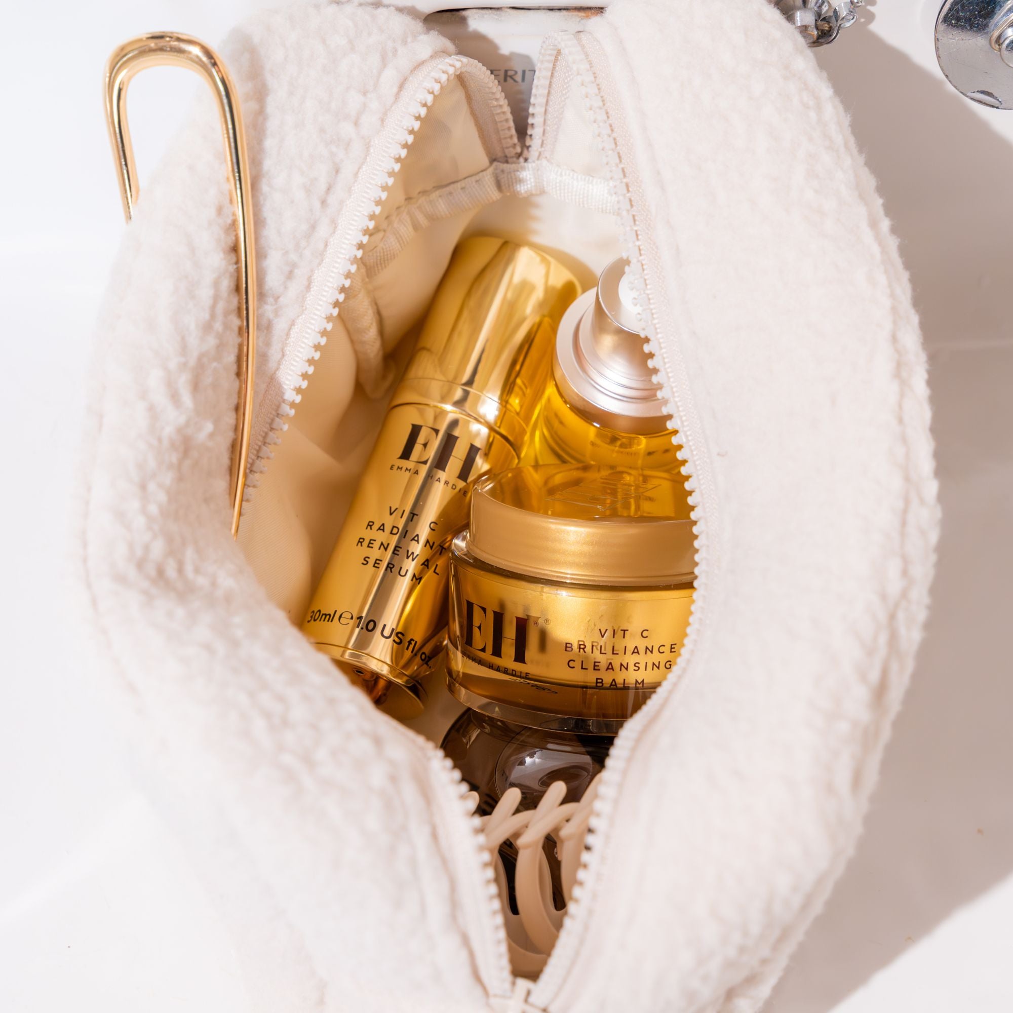 Emma Hardie Vit C skincare products nestled inside a soft white make-up bag, including Radiant Renewal Serum, Brilliance Facial Oil and Vit C Brilliance Cleansing Balm.