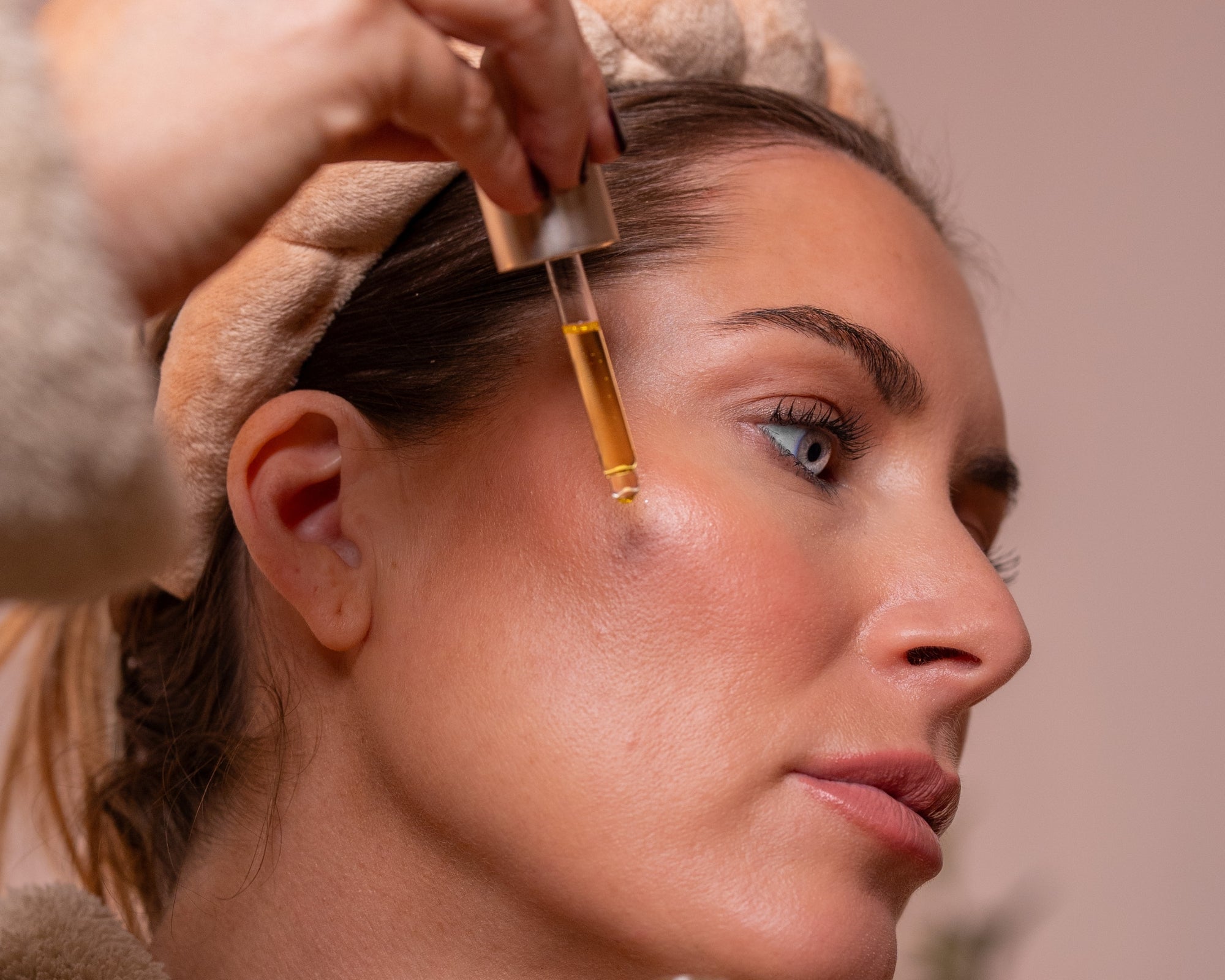 Woman applying Emma Hardie Brilliance Facial Oil to her cheek with a dropper as part of a hydrating skincare ritual.