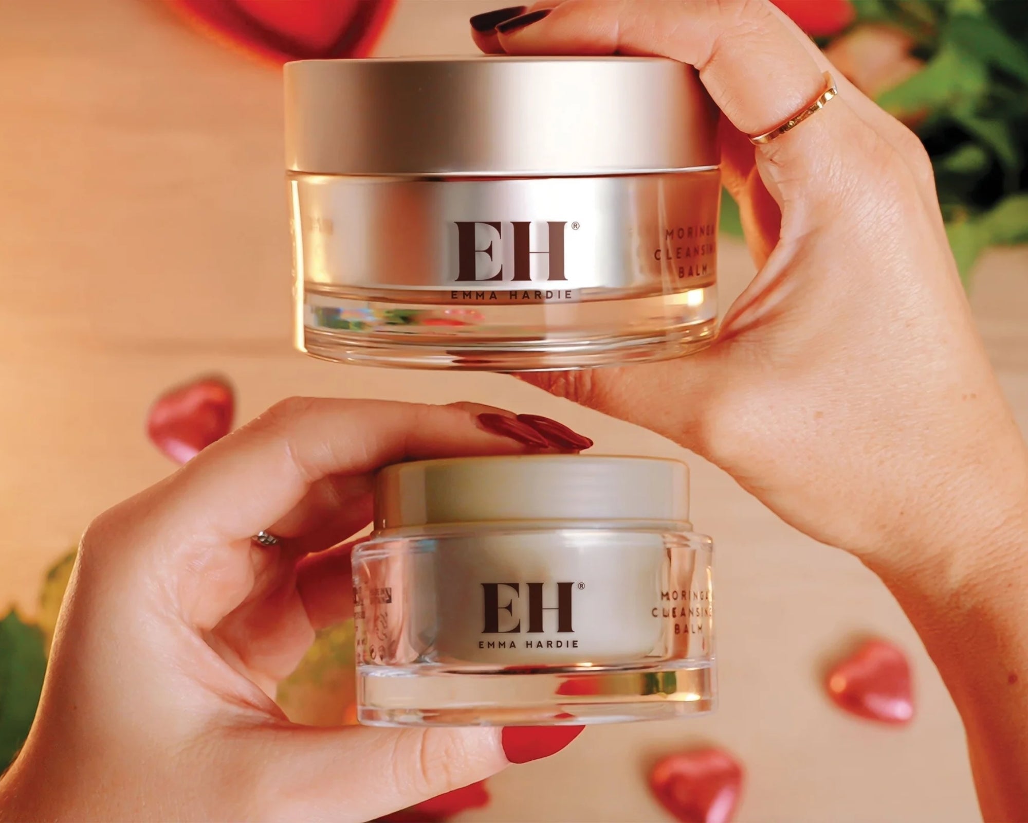 Two Emma Hardie Moringa Cleansing Balms held in hand, showing two jar sizes against a warm botanical background.