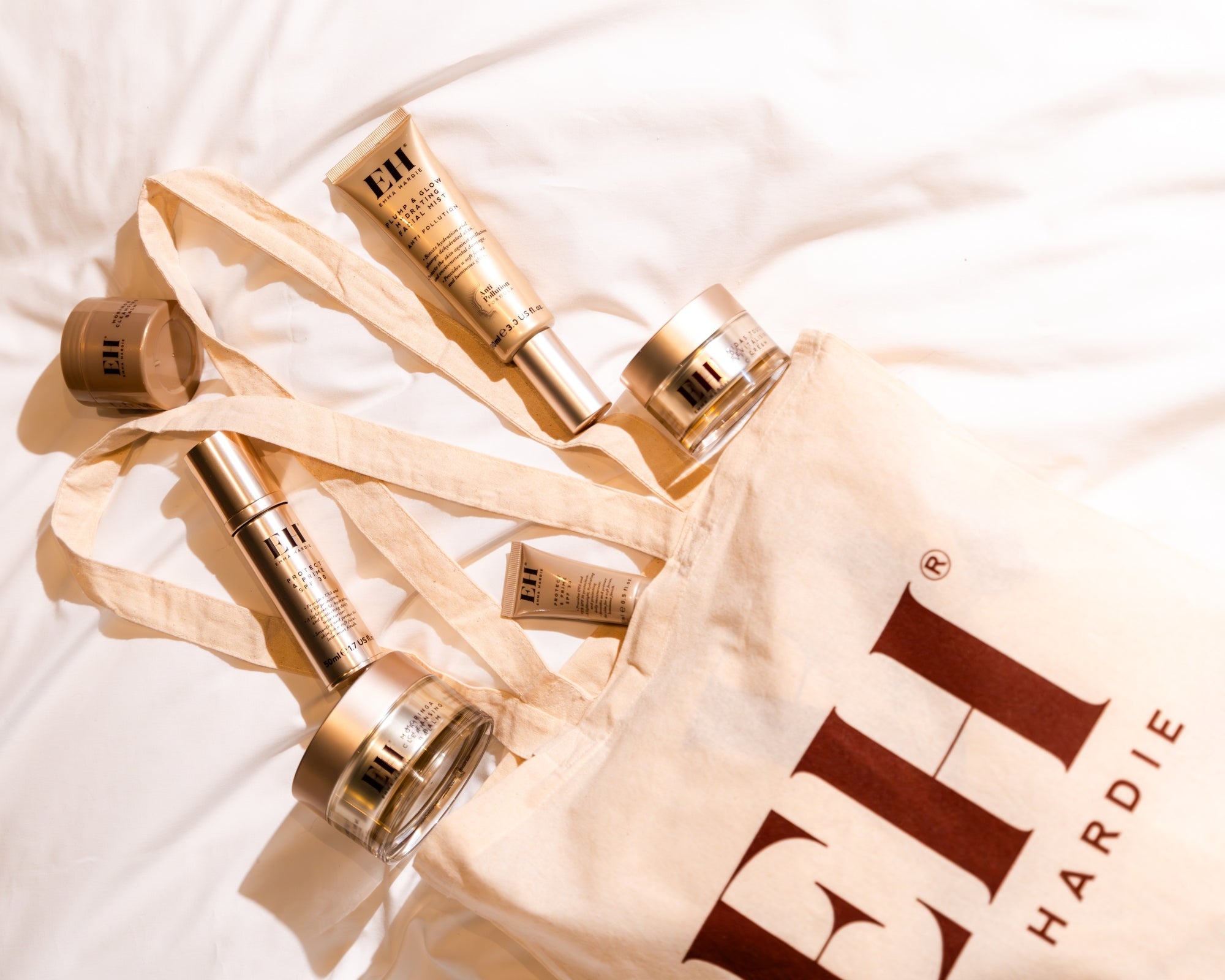 Emma Hardie skincare products in a branded canvas tote bag, styled on soft white bedding for an at-home skincare ritual.