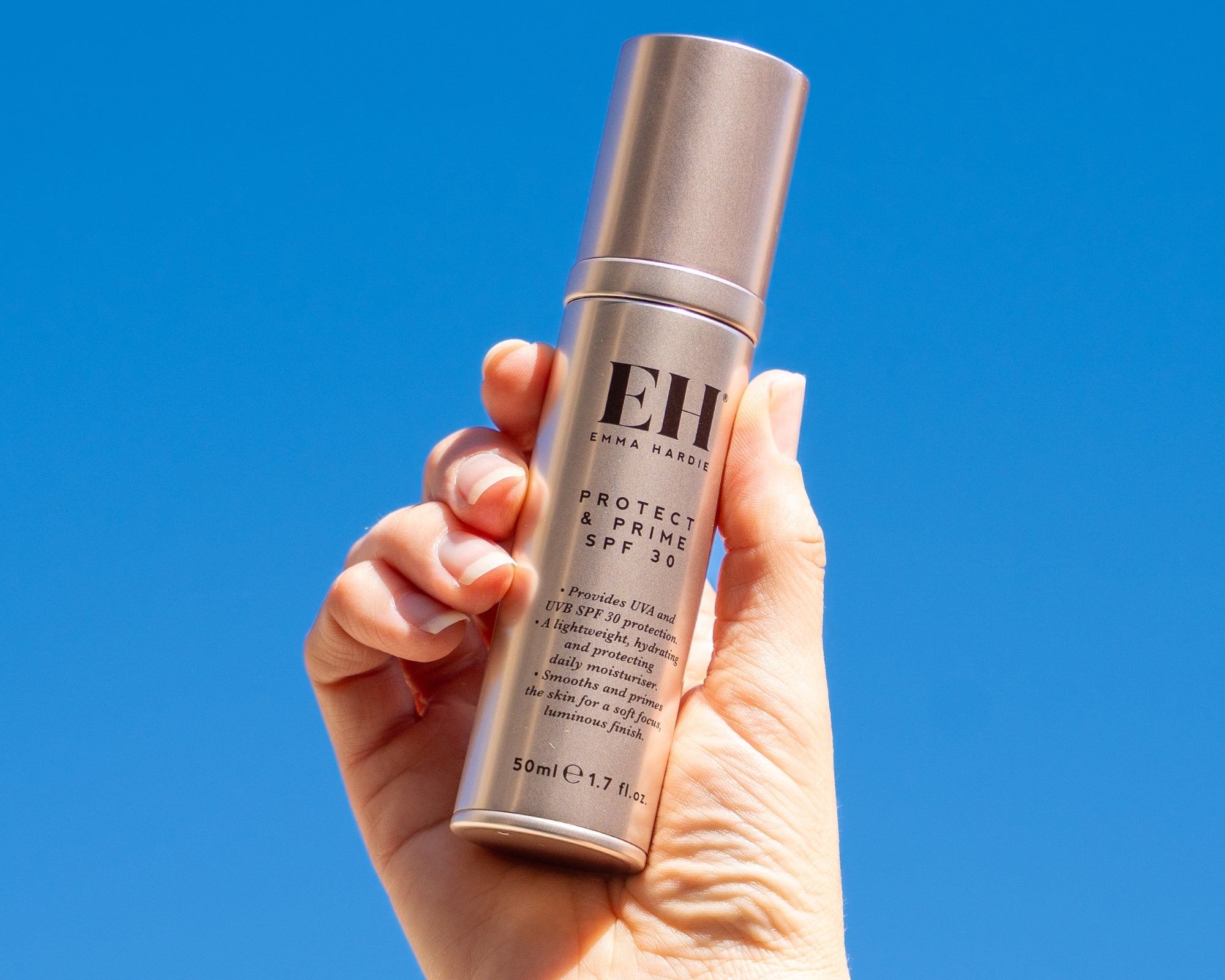Emma Hardie Protect & Prime SPF30 held in hand against a bright blue background