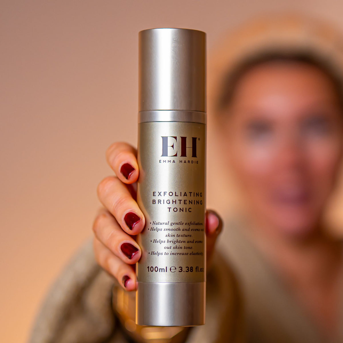 Exfoliating Brightening Tonic held towards the camera with a softly blurred model behind.