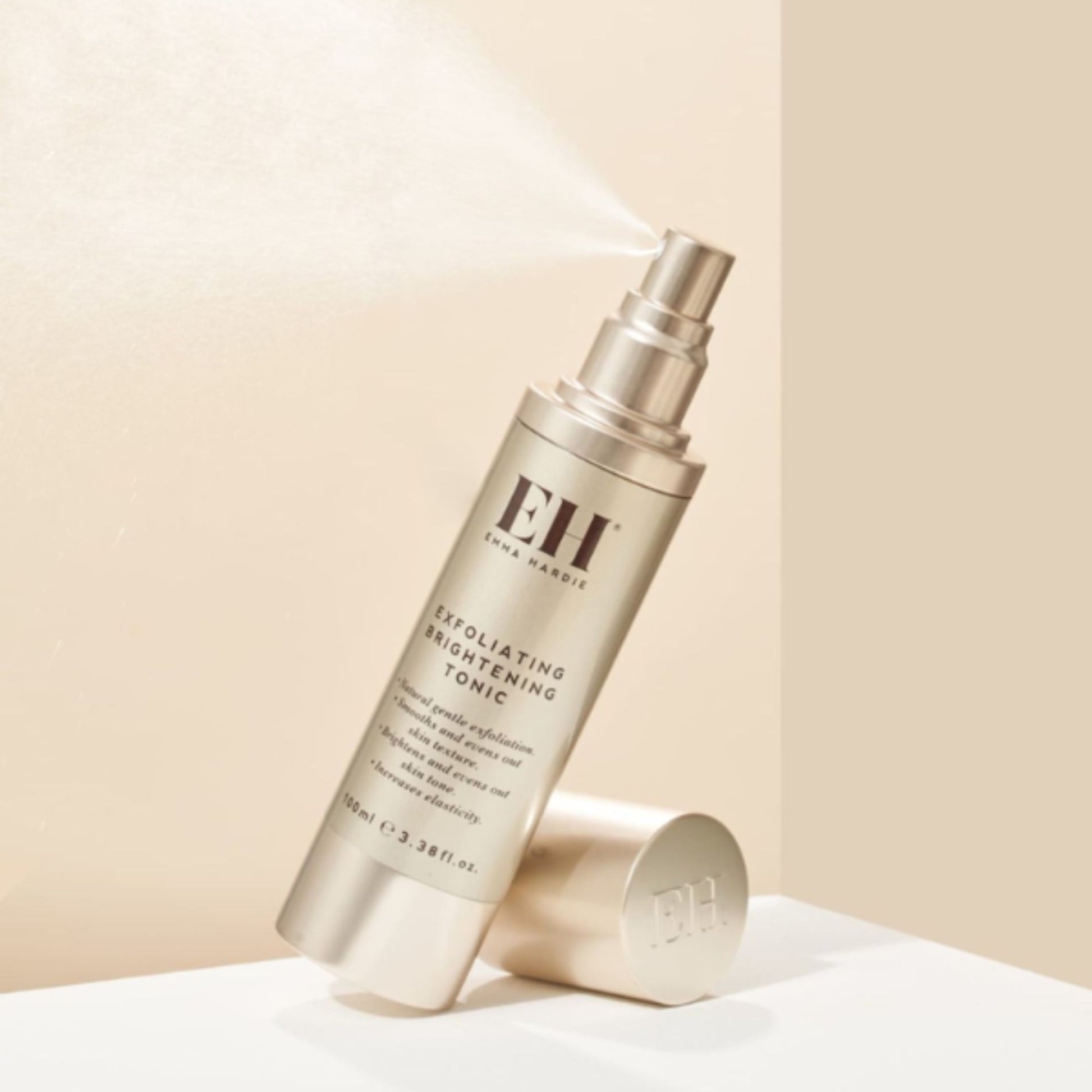 Emma Hardie Exfoliating Brightening Tonic bottle spraying a fine mist against a soft neutral background, with the cap placed beside it.