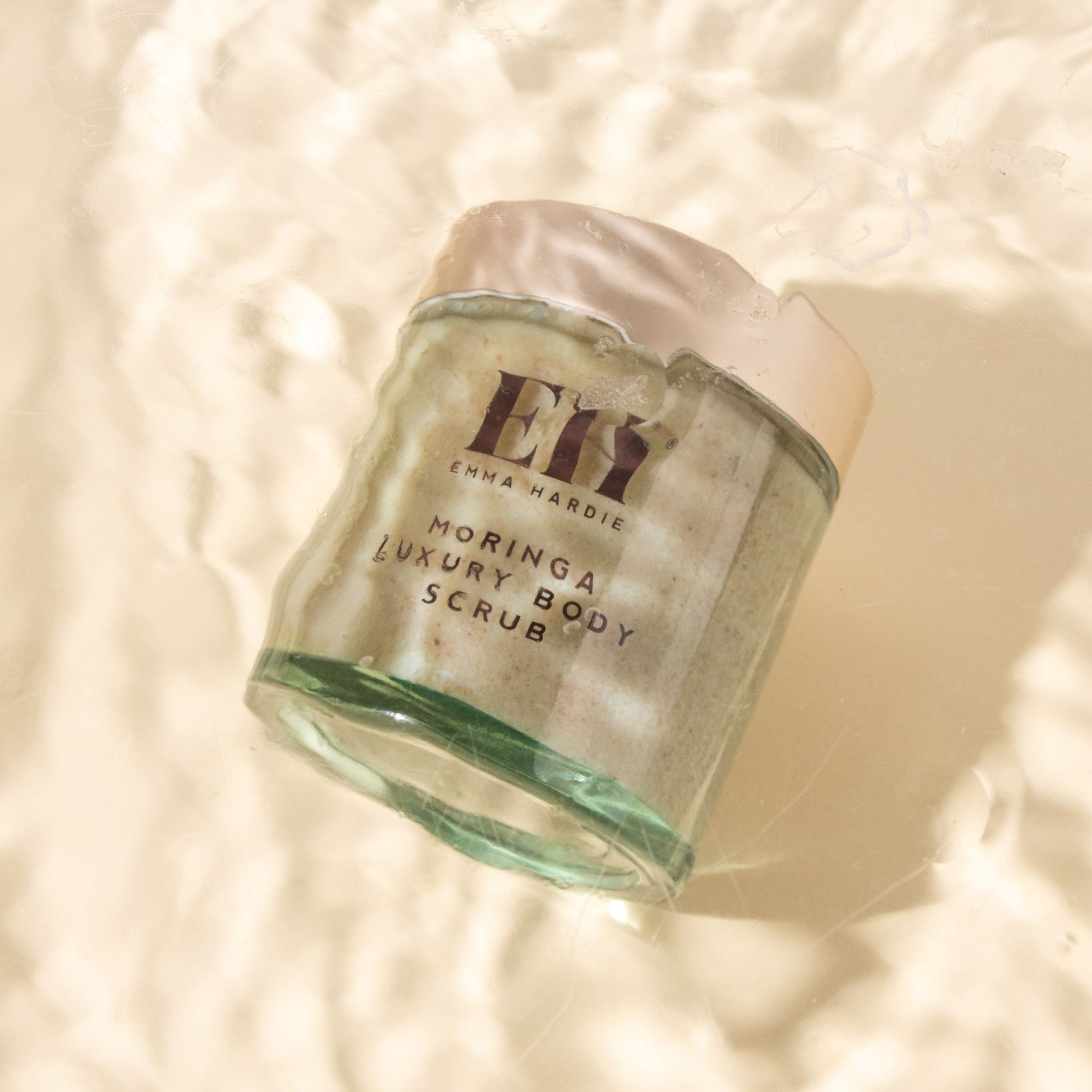 Emma Hardie Moringa Luxury Body Scrub jar surrounded by soft golden water reflections, highlighting the sensorial body care texture.