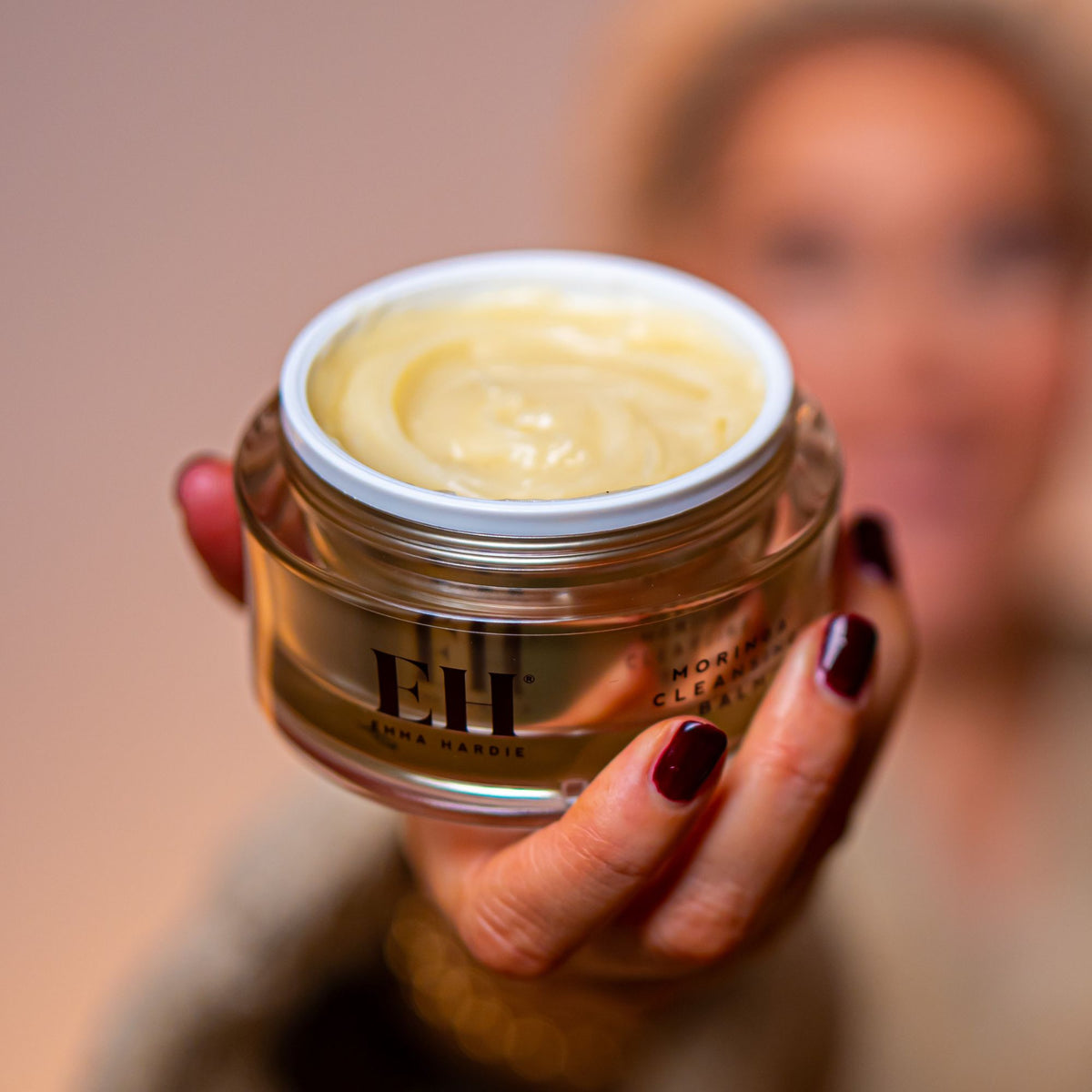 Moringa Cleansing balm held towards the camera with a softly blurred model behind.