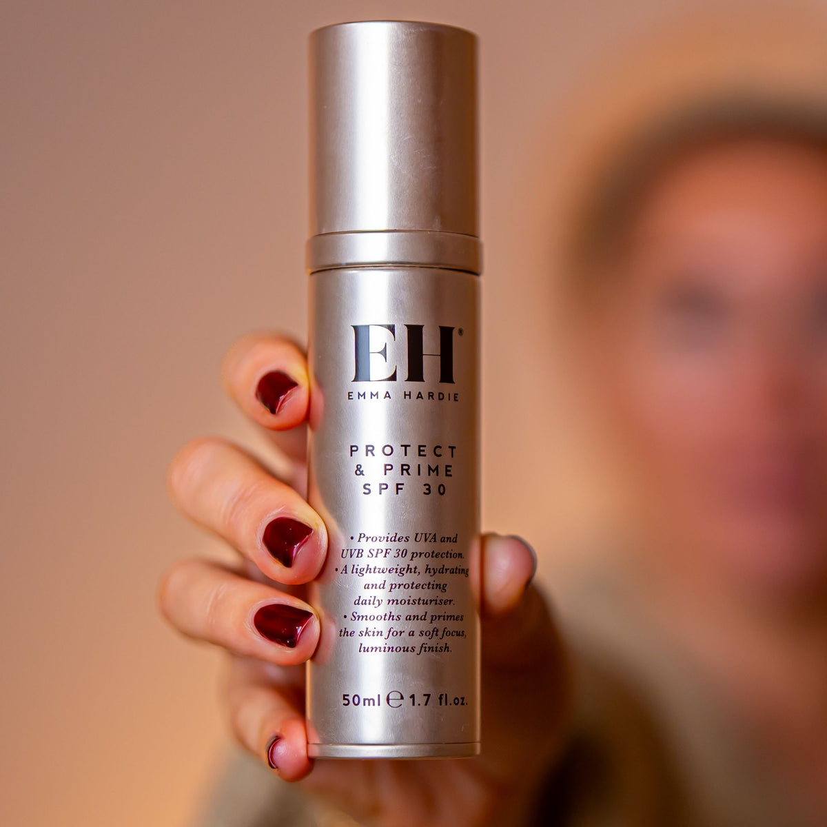 Protect & Prime SPF 30 held towards the camera with a softly blurred model behind.