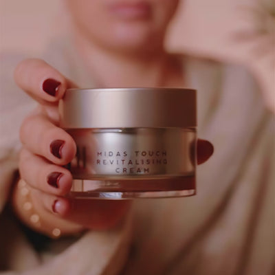 Woman showing jar of Midas Touch Revitalising Cream, then applying the cream. 